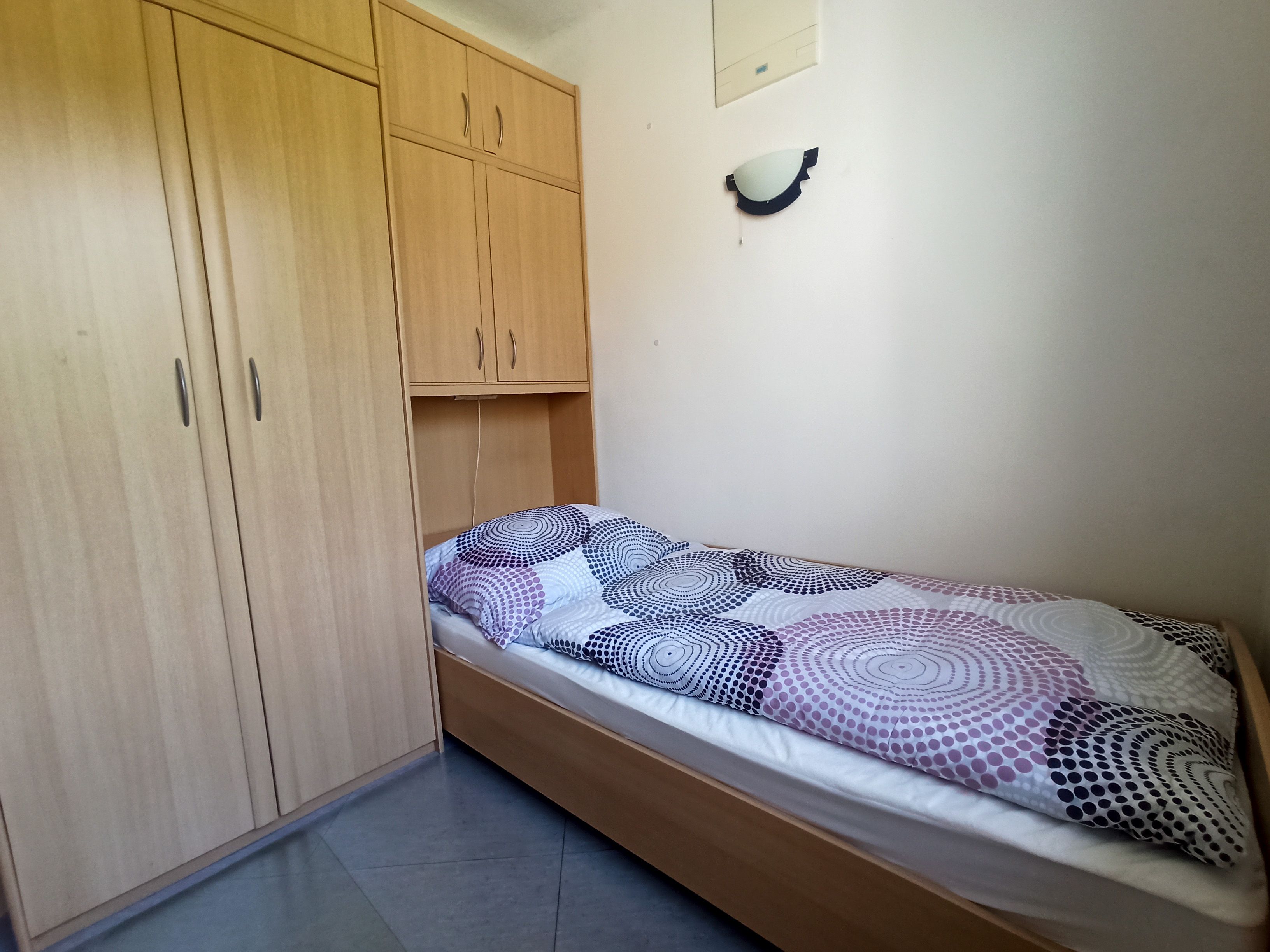 Ein einfaches Schlafzimmer mit einem Einzelbett und einem großen Holzschrank.