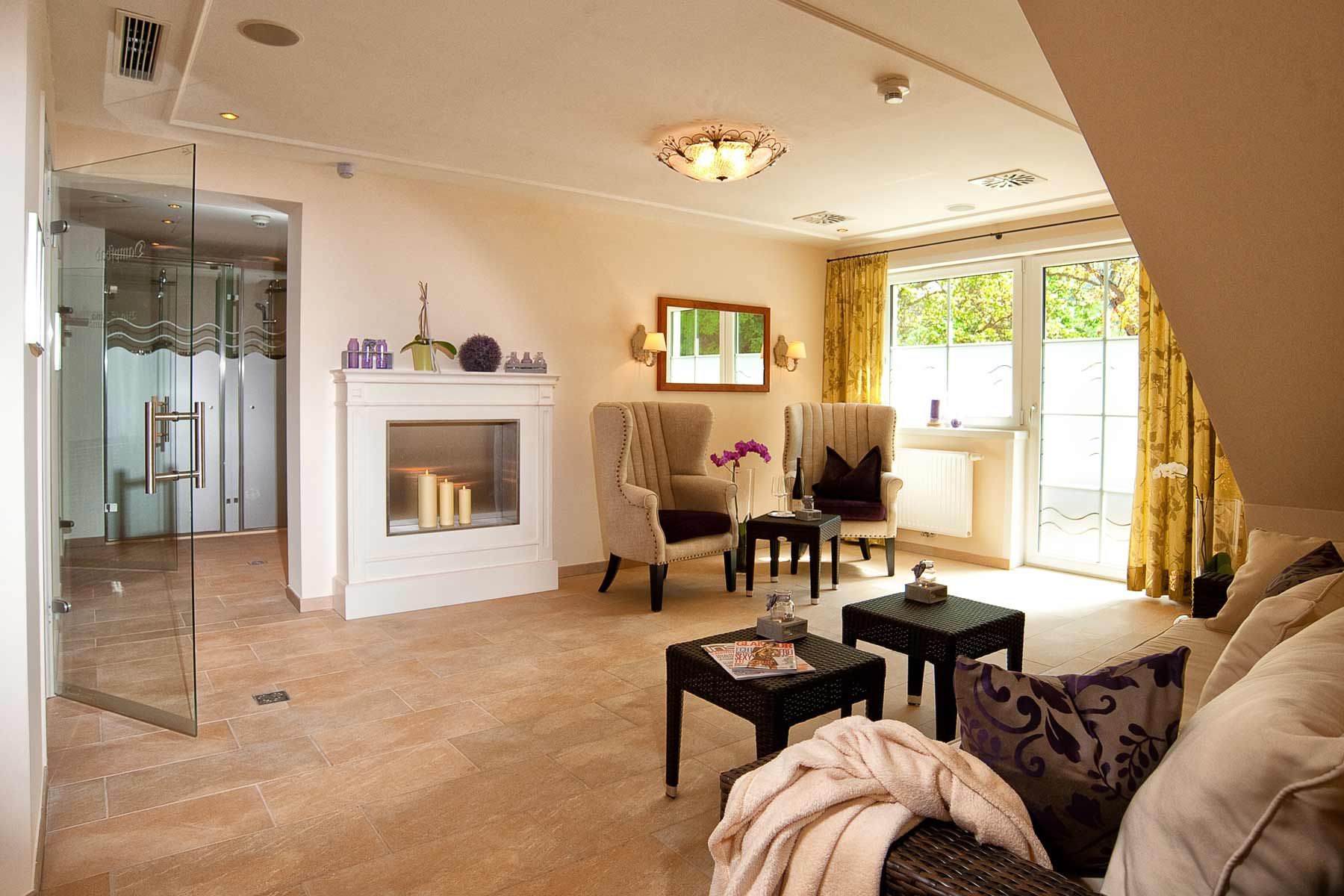 Eleganter Wellnessbereich mit Kamin, Sesseln und Glastür.