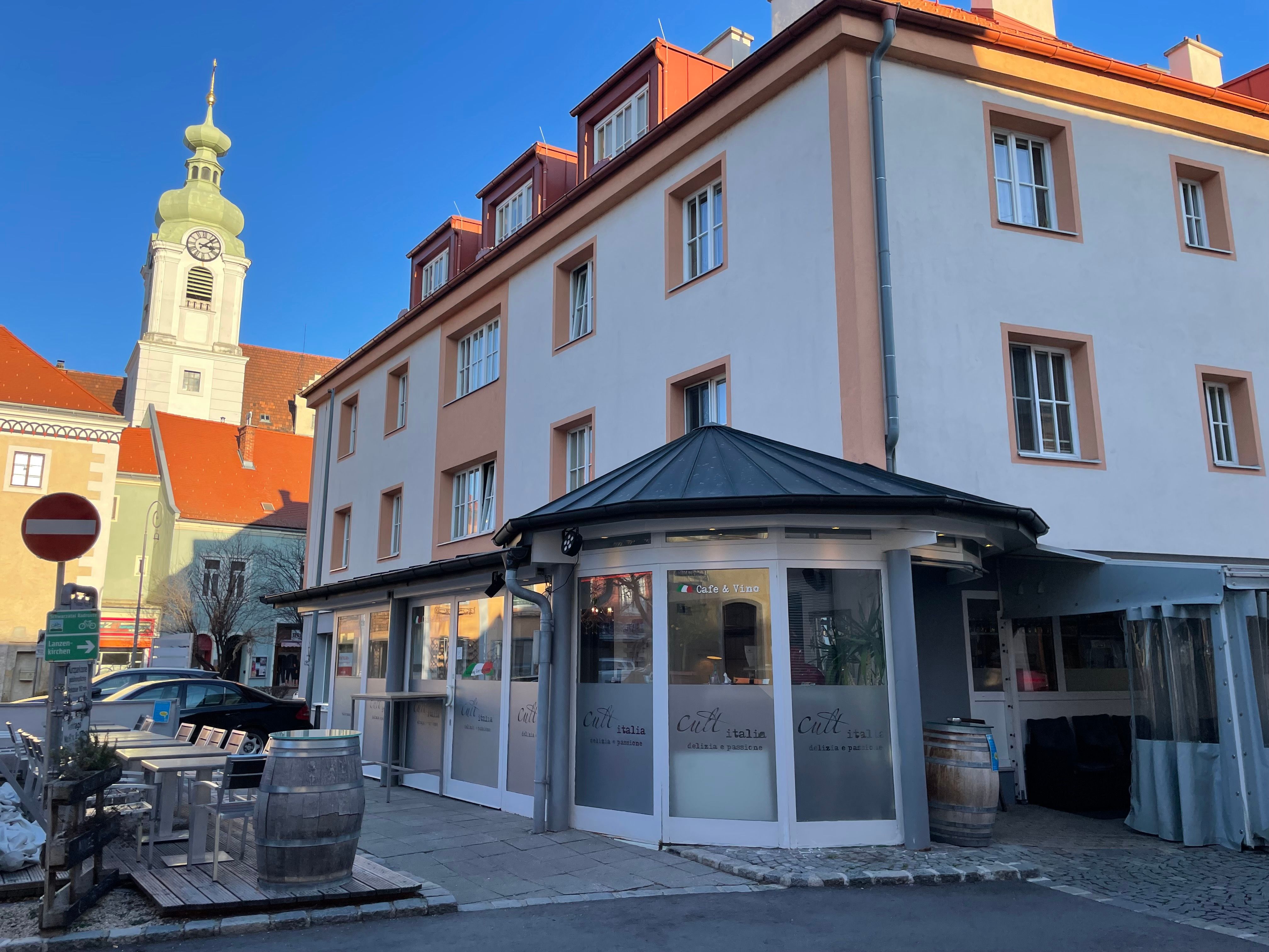 Außenansicht eines Restaurants mit der Aufschrift 'Cult Italia' und einem Kirchturm im Hintergrund.