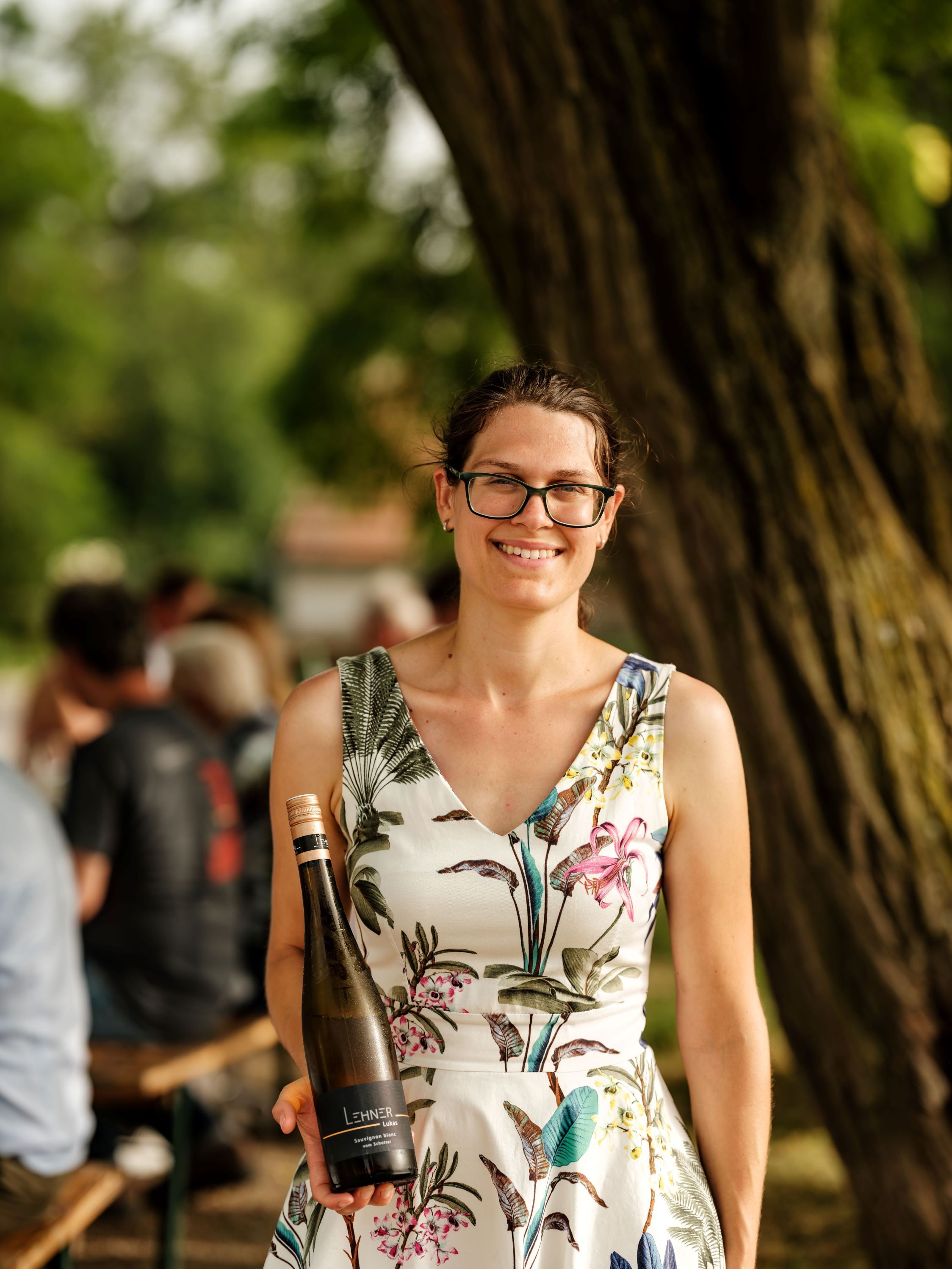 Frau mit Brille hält eine Weinflasche im Freien.