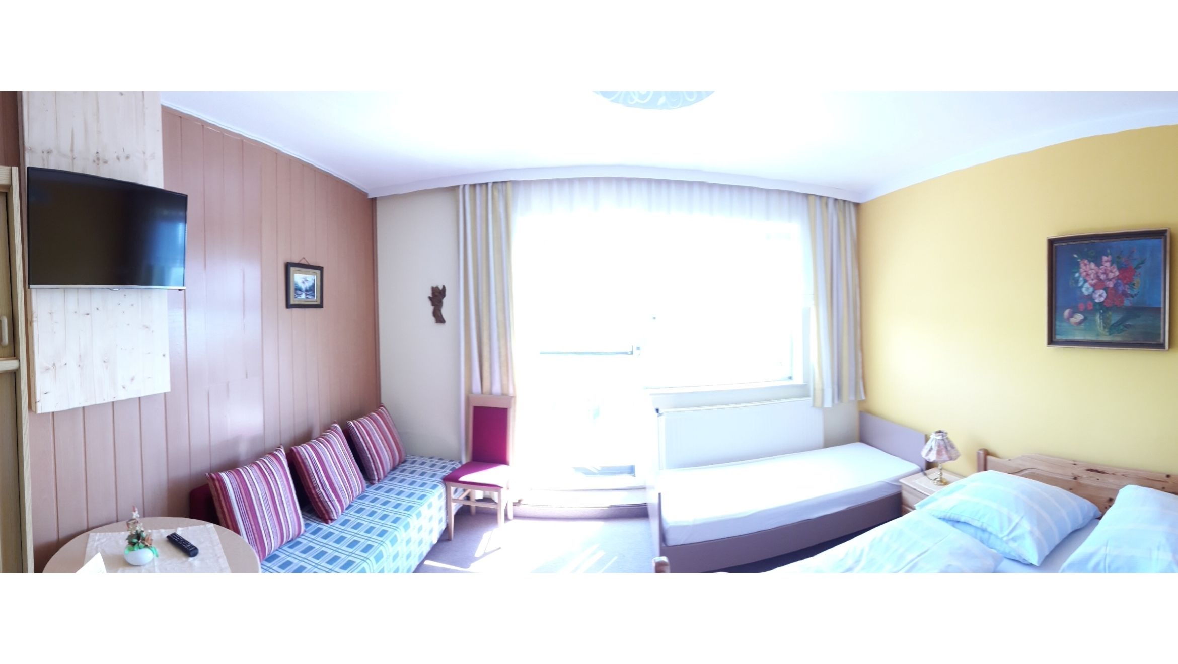 Ein helles Gästezimmer mit Sofa, Bett, Fernseher und Gemälde an der Wand.