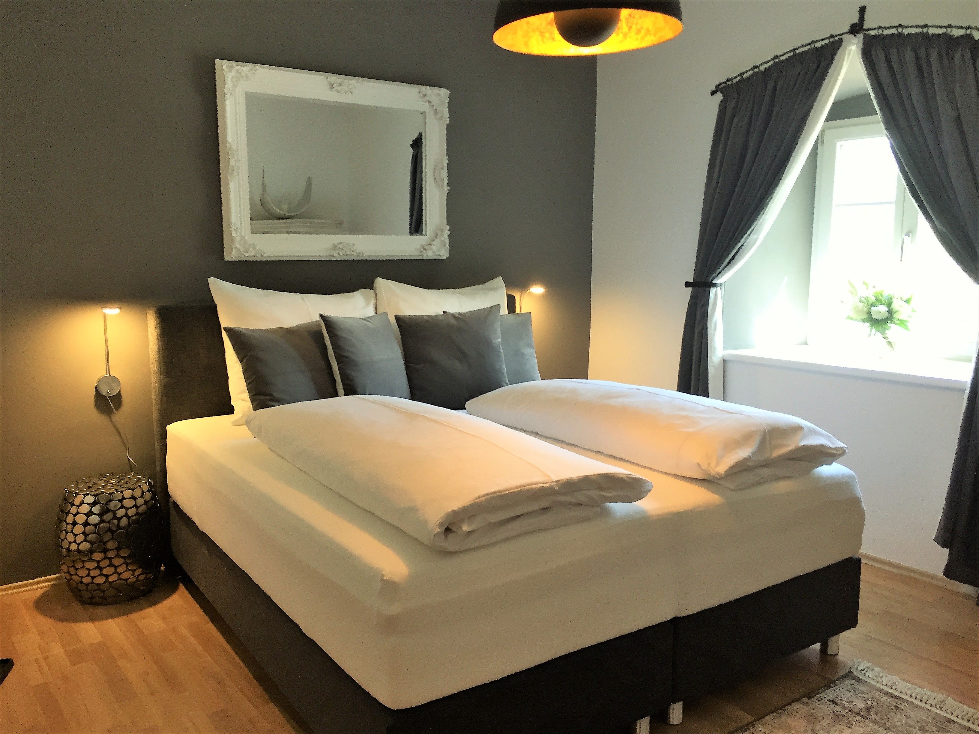 Modernes Schlafzimmer mit Doppelbett, grauen Wänden und dekorativem Spiegel.