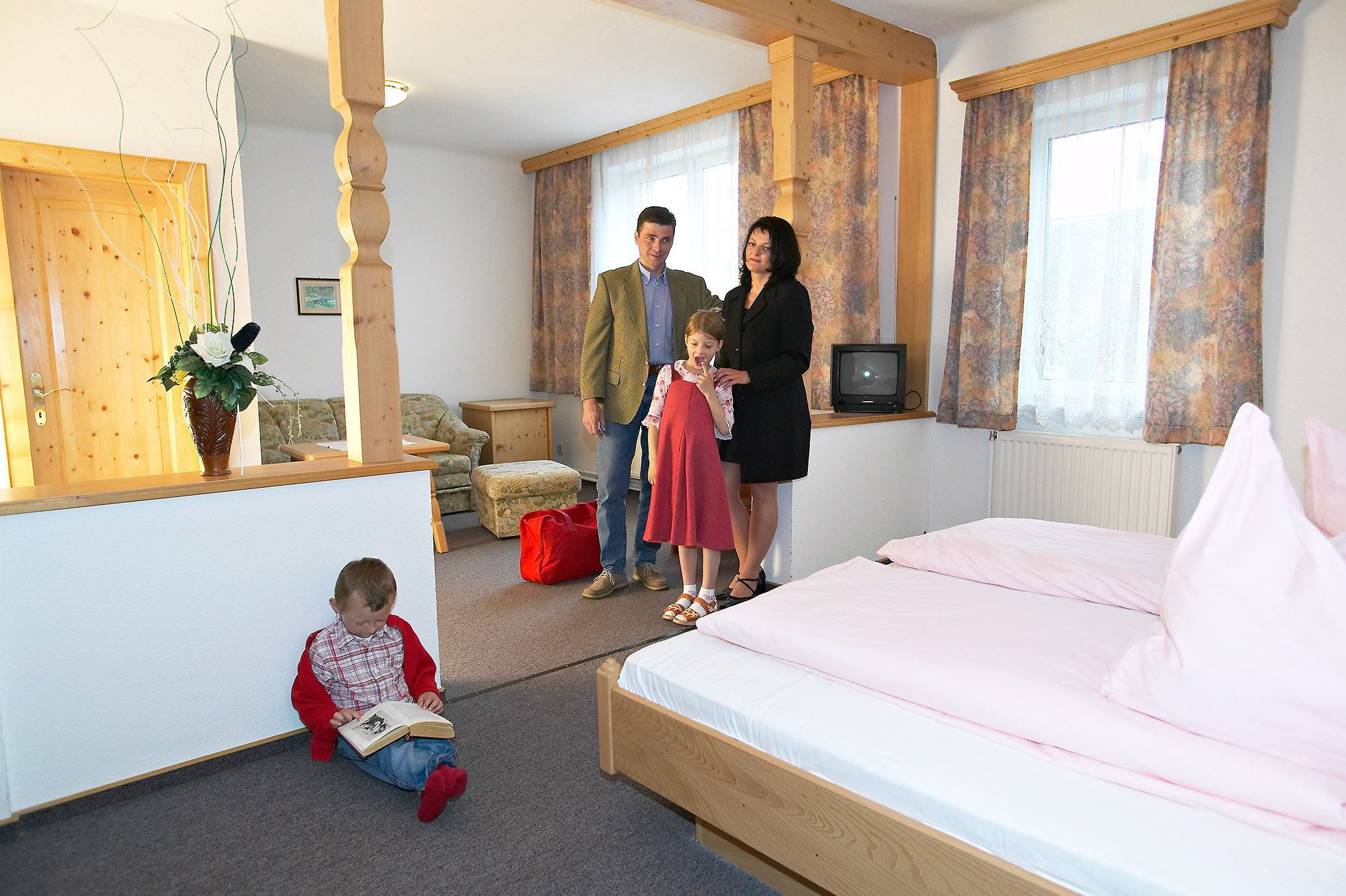 Familie in einem gemütlichen Hotelzimmer mit Holzmöbeln und rosa Bettwäsche.