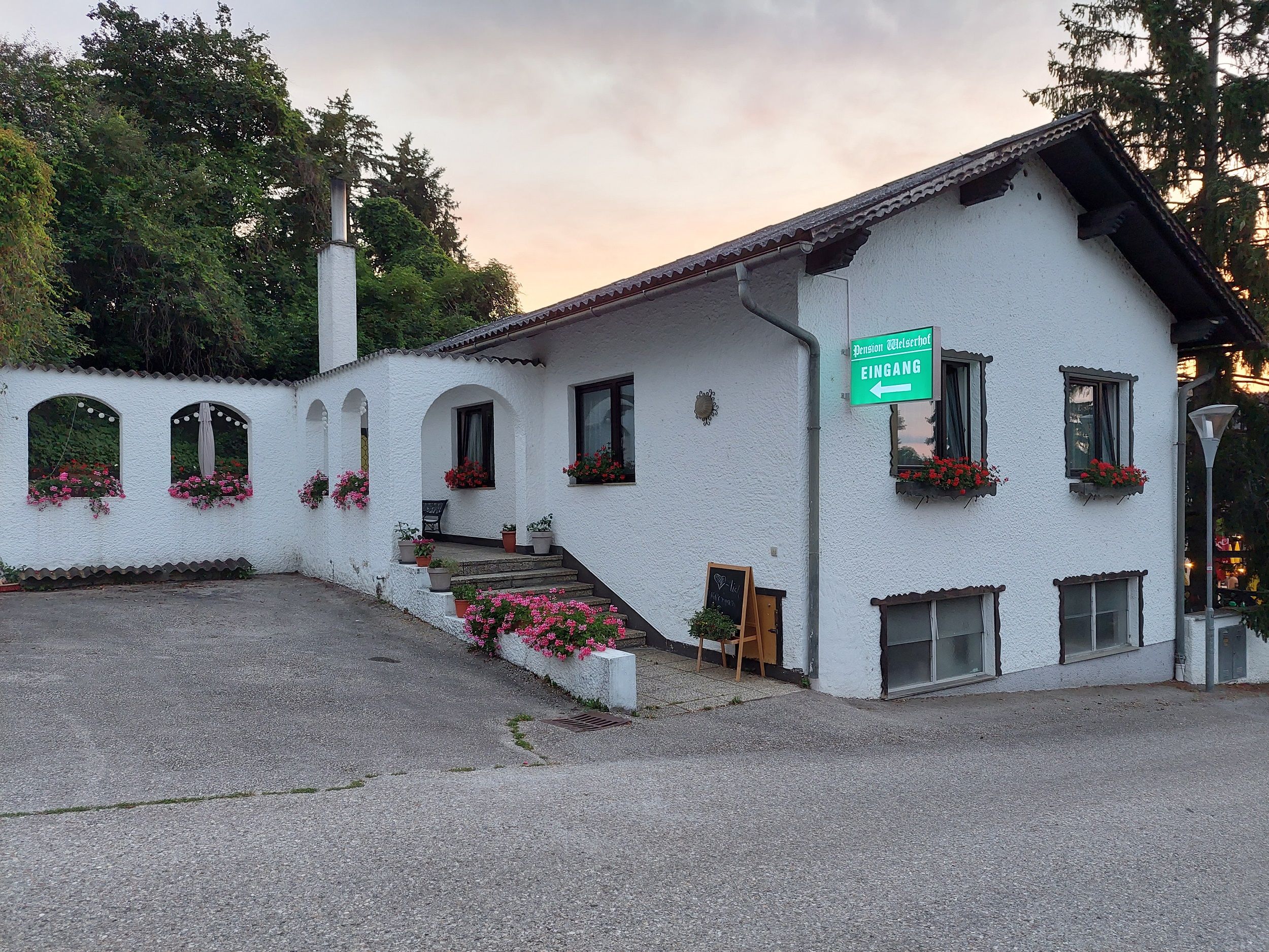 Außenansicht eines weißen Gebäudes mit Blumen und einem Schild "Pension Welserhof Eingang".