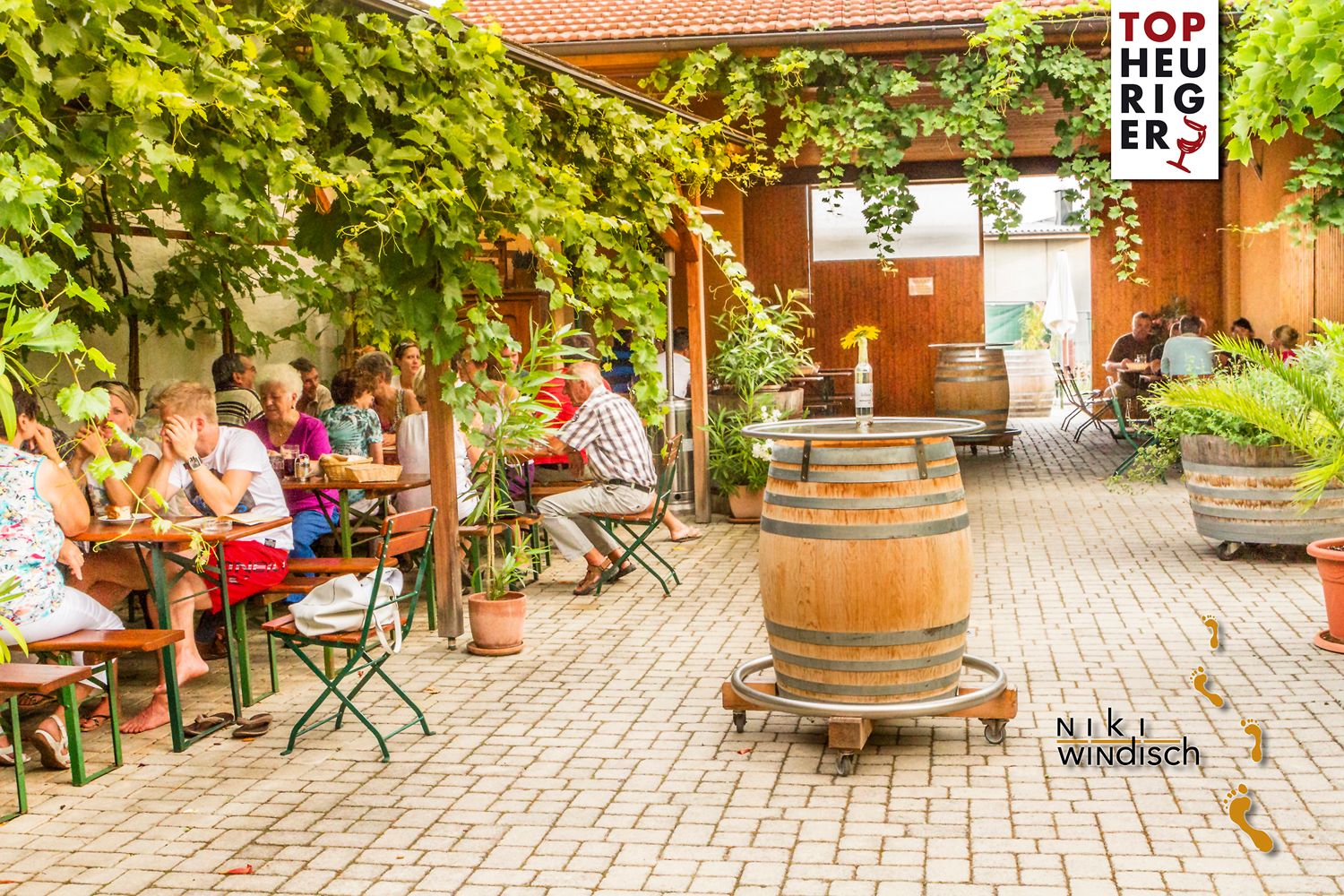 Ein gemütlicher Heuriger mit Gästen unter einer Laube aus Weinreben.