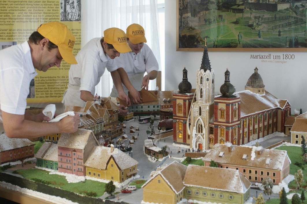 Drei Personen dekorieren ein Lebkuchenmodell von Mariazell um 1800.