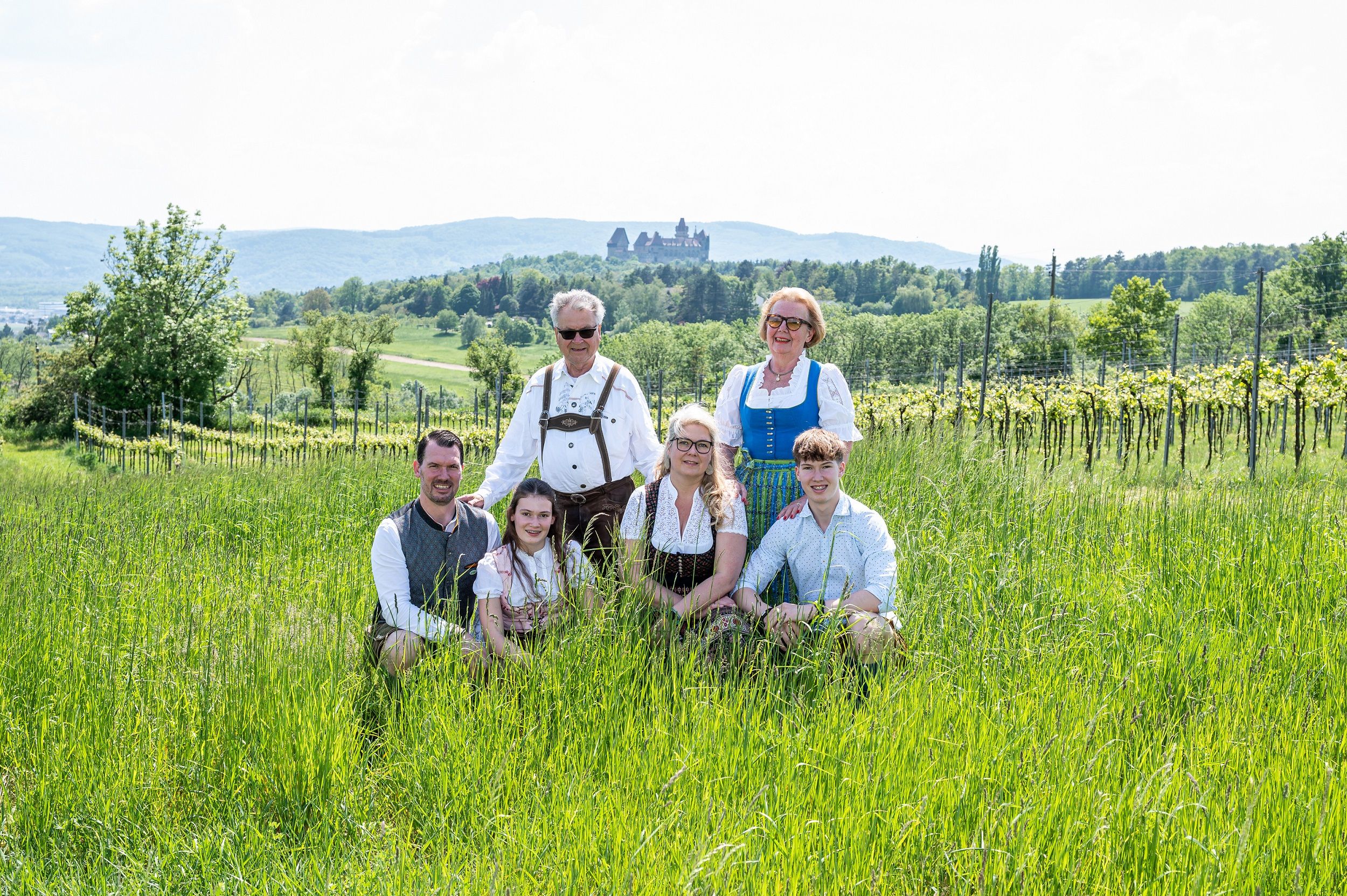 Eine Familie in traditioneller Kleidung posiert auf einer Wiese mit einem Schloss im Hintergrund.