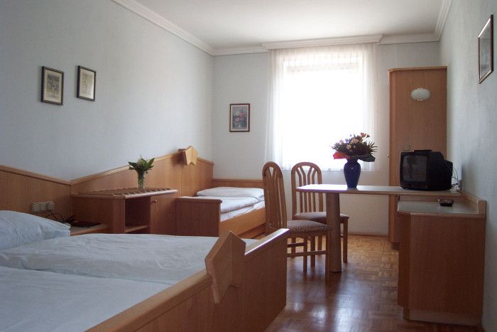 Ein einfach eingerichtetes Hotelzimmer mit zwei Betten, einem Tisch, Stühlen und einem kleinen Fernseher.