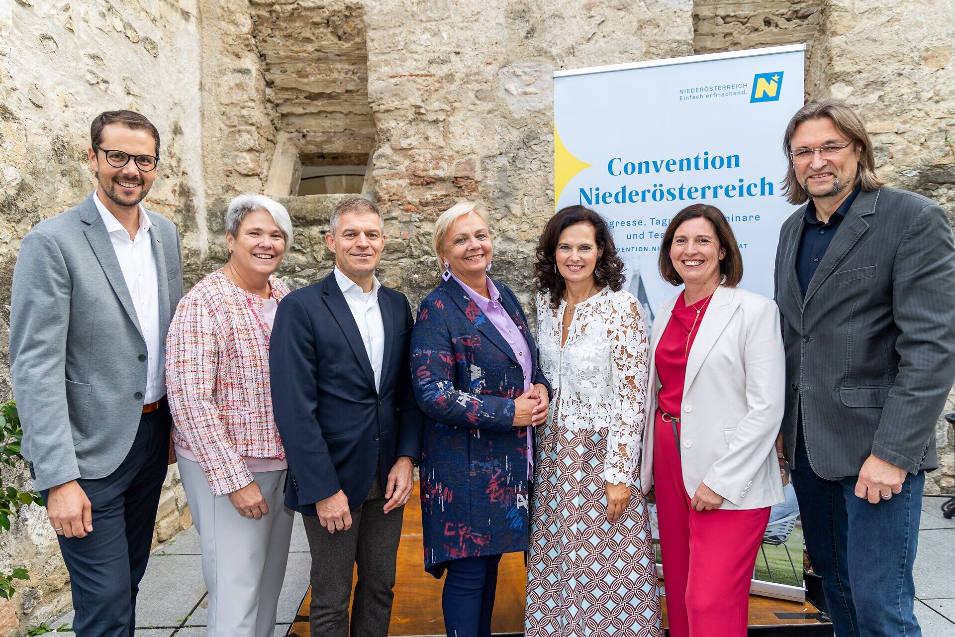 Gruppenfoto beim Jubiläumsevent des Convention Bureau Niederösterreich in Perchtoldsdorf: Marcus Linford, Michaela Zeiler, Christian Neuwirth, Andrea Kö, Edith Mader, Maria-Luise Fröch und Thomas Denk vor einem Convention-Niederösterreich-Roll-up.