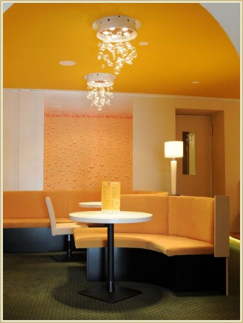 Innenansicht eines modernen Cafés mit gelben Wänden, runden Tischen und gepolsterten Sitzbänken.