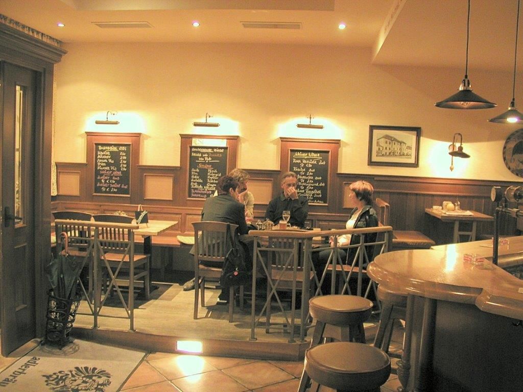 Innenansicht eines gemütlichen Gasthauses mit Holzmöbeln und drei Personen an einem Tisch.