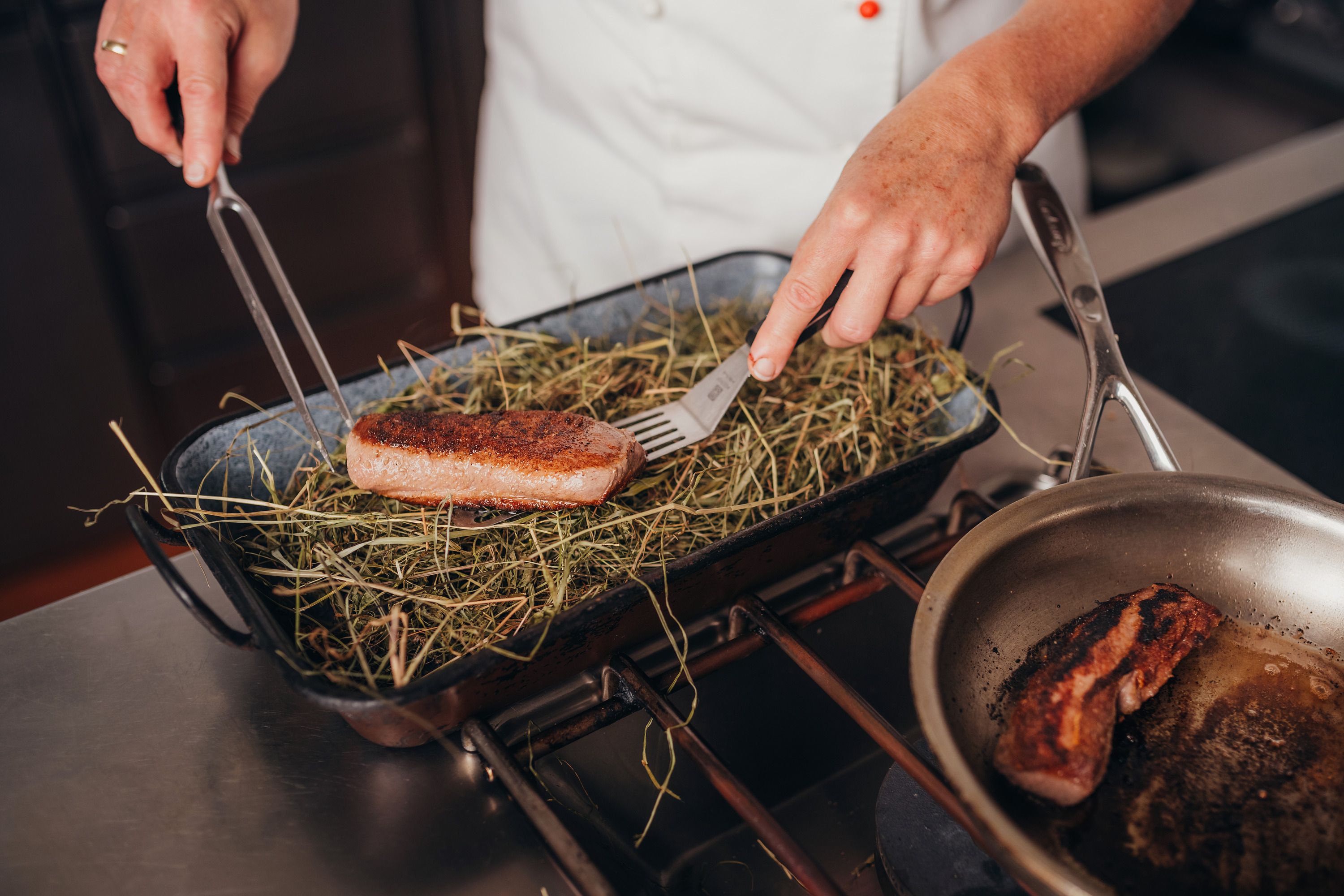 Ein Koch legt ein Stück Hirschrücken auf ein Bett aus Heu in einer Bratform.