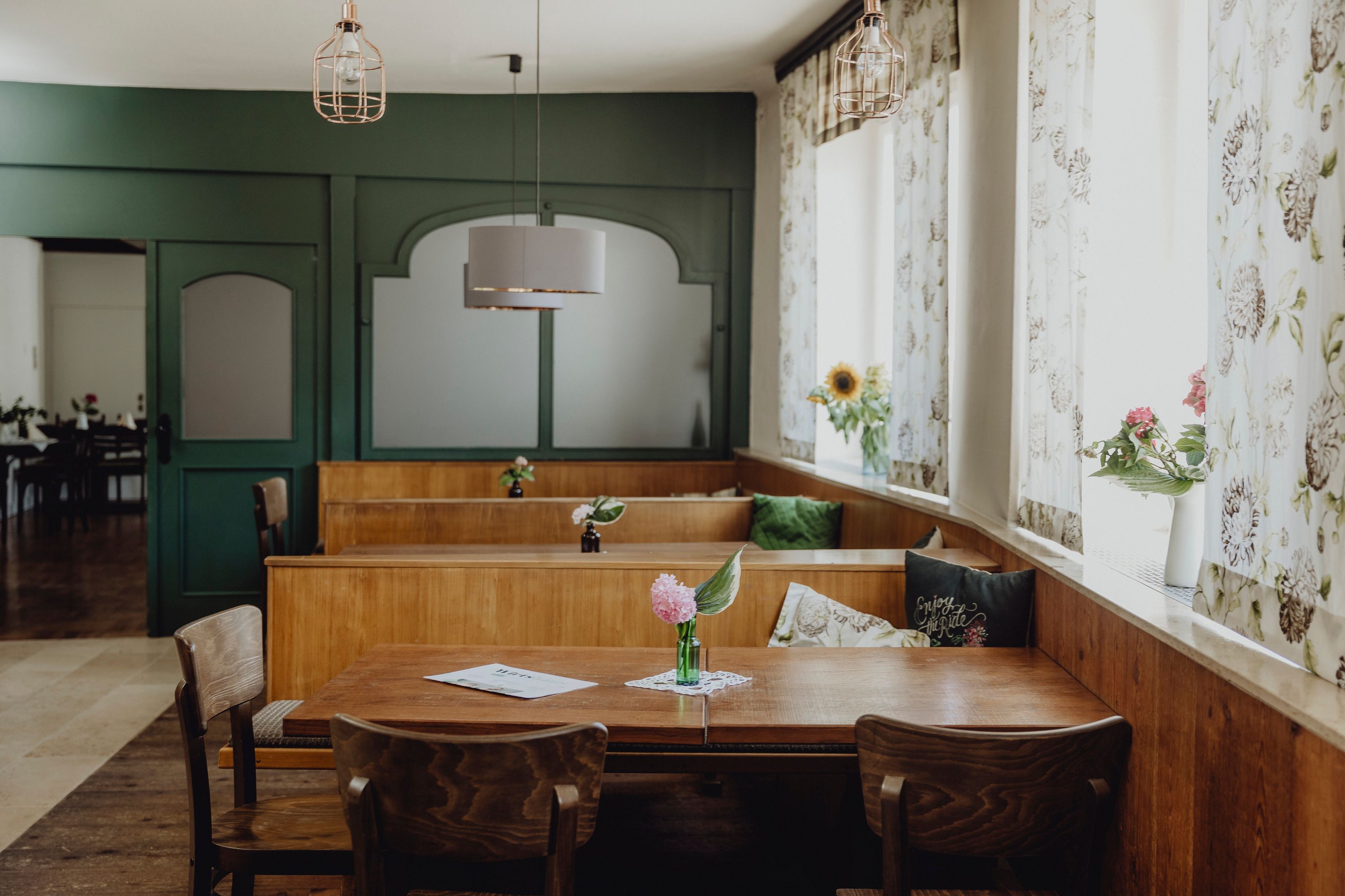 Innenansicht eines traditionellen Wirtshauses mit Holzmöbeln und Blumen auf den Tischen.