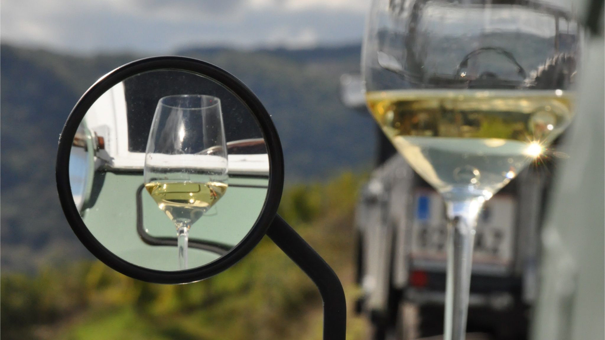 Ein Weinglas mit Weißwein im Rückspiegel eines Autos