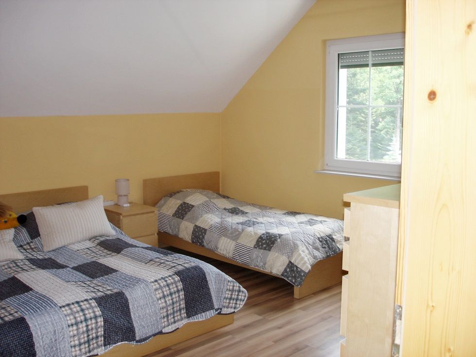 Zwei Einzelbetten in einem gelb gestrichenen Schlafzimmer mit Dachschräge und Fenster.