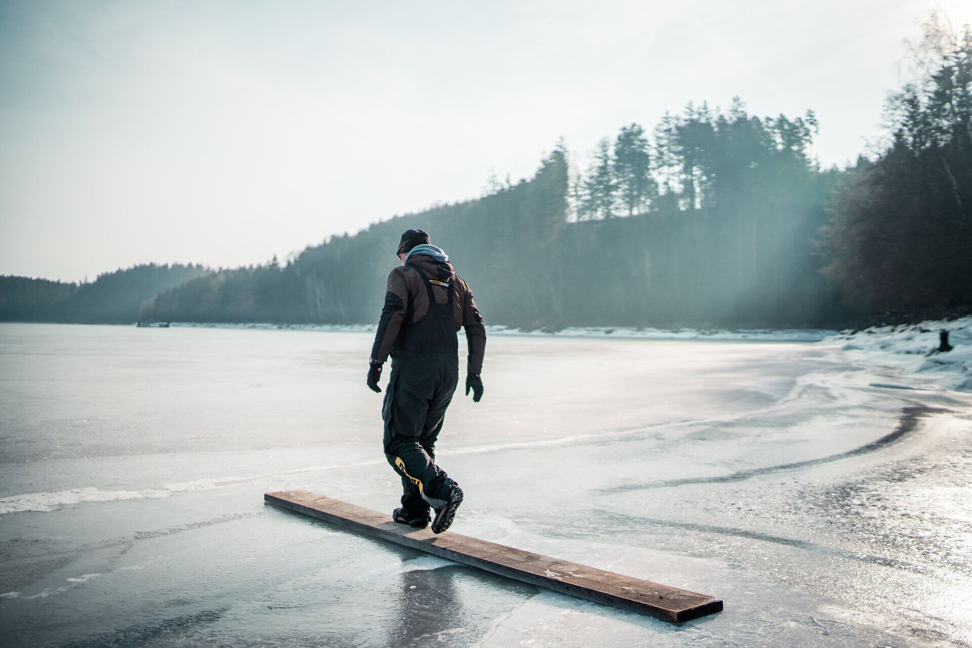Ein Fischer balanciert geschickt auf einem schmalen Holzbrett über die glitzernde Eisfläche des Stausees. Die ruhige Winterlandschaft, umgeben von schneebedeckten Bäumen, schafft eine friedliche Atmosphäre, die zum Verweilen einlädt. Hier, wo die Natur in ihrer stillen Pracht erstrahlt, wird das Eisfischen zu einem unvergesslichen Erlebnis.