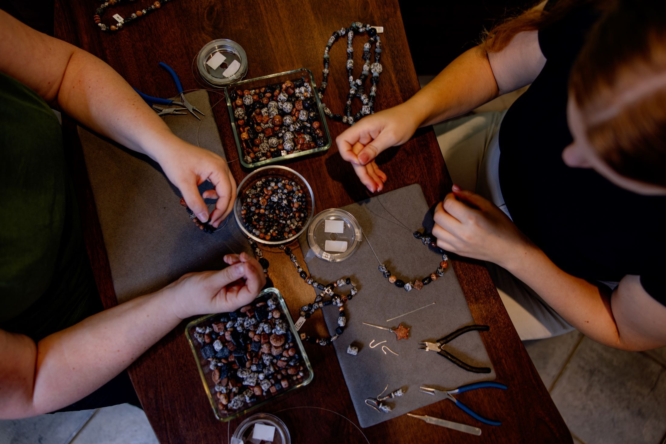 Zwei Personen fertigen Granitschmuck an einem Tisch mit Perlen und Werkzeugen.