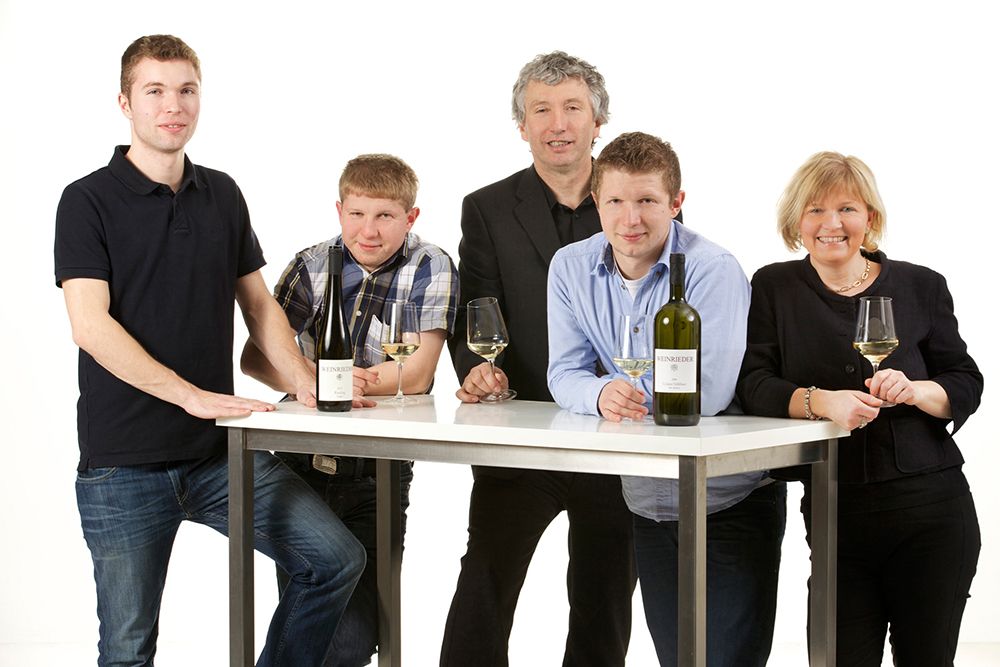 Fünf Personen stehen um einen Tisch mit Weinflaschen und Gläsern.