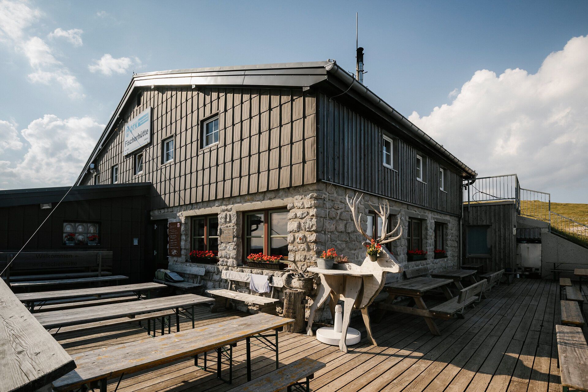 Fischerhütte am Schneeberg mit Terrasse, Sitzbänken und dekorativer Steinbockfigur vor dem Gebäude