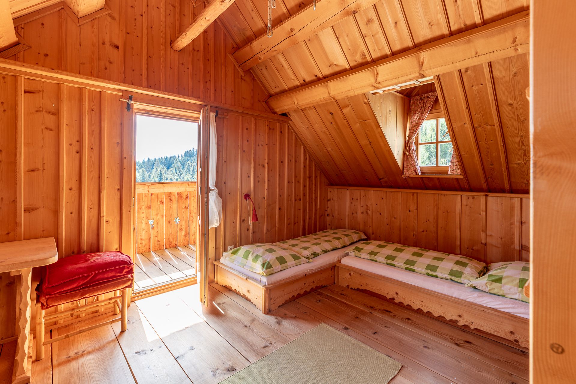 Schlafzimmer mit Holzvertäfelung, zwei Betten, einem Fenster und offener Tür zum Balkon.