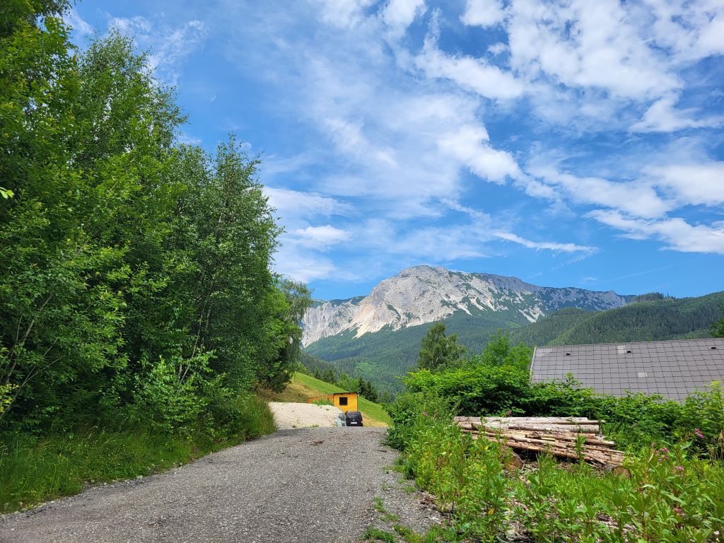 Zufahrt zu einem Tinyhouse in einer bergigen Landschaft mit blauem Himmel und Wolken.