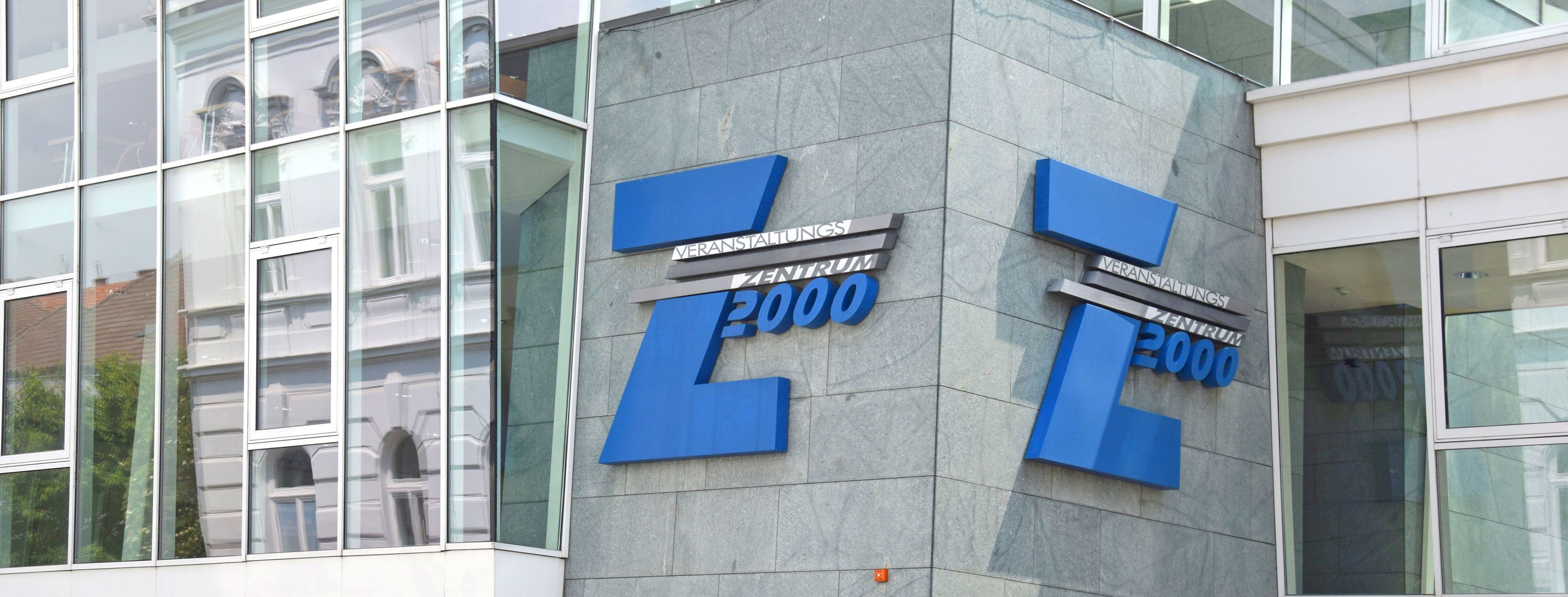Eingang des Veranstaltungszentrums Z2000 mit blauem Logo auf grauer Fassade.
