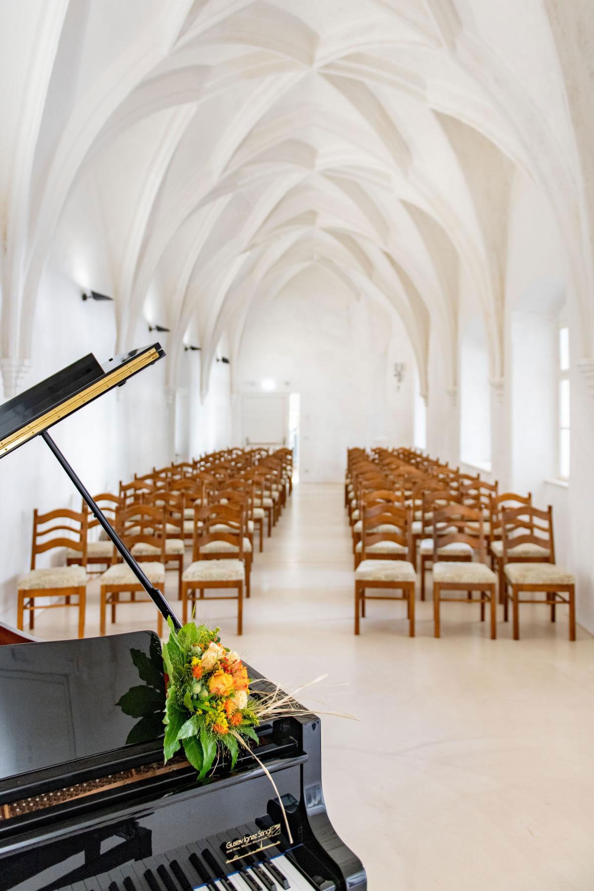 Ein Flügel mit Blumenarrangement steht in einer gotischen Halle mit gewölbter Decke und Reihen von Holzstühlen.