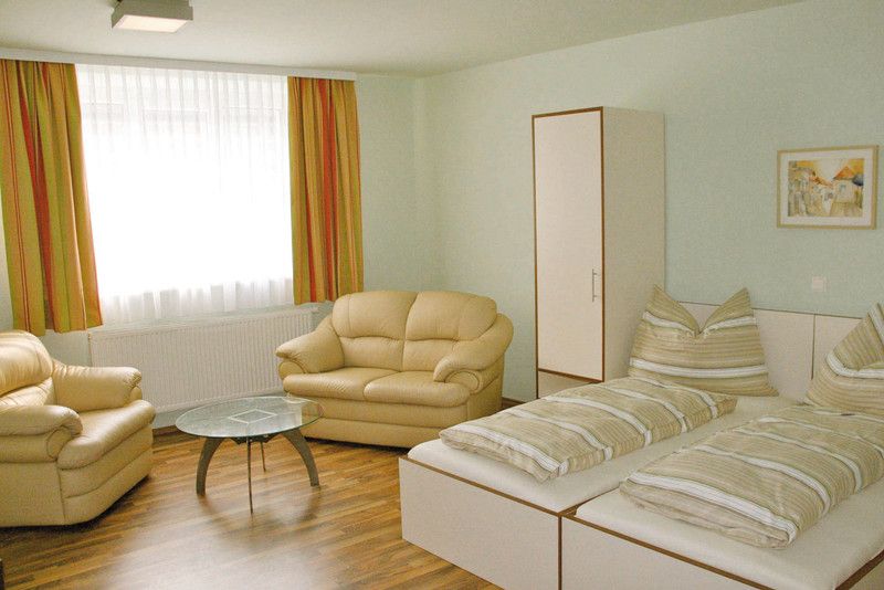 Helles Zimmer mit zwei Betten, Sofas, einem Tisch und einem Schrank.