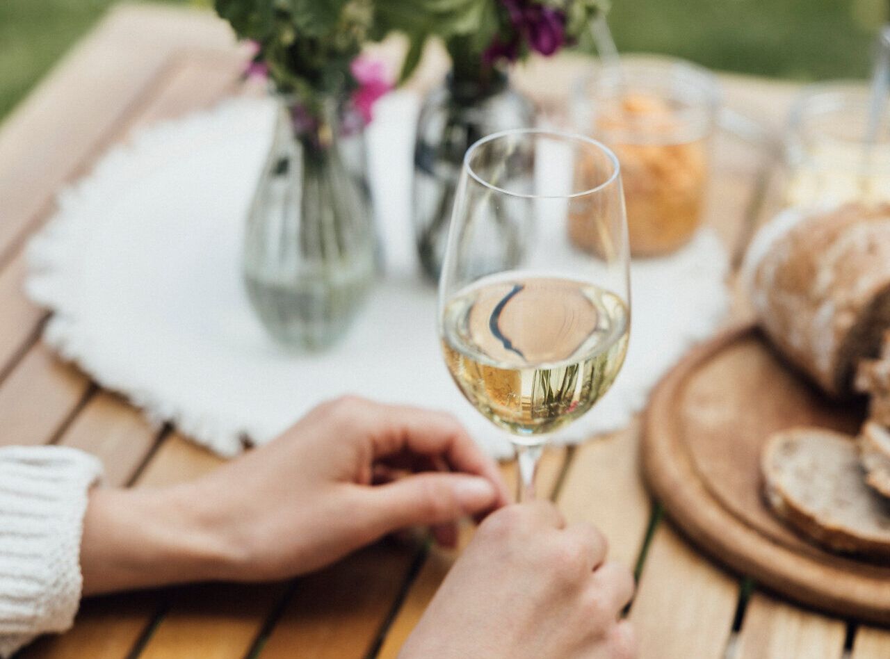 Ein sonniger Nachmittag auf einem malerischen Winzerhof, wo die Gäste mit einem Glas frischem Wein anstoßen. Umgeben von blühenden Wildblumen und einer einladenden Jause, genießen die Besucher die entspannte Atmosphäre und die köstlichen Aromen der Region.