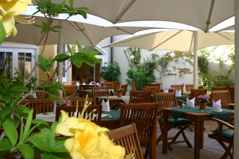 Ein gemütlicher Gastgarten mit Holzmöbeln und Sonnenschirmen, umgeben von Pflanzen.