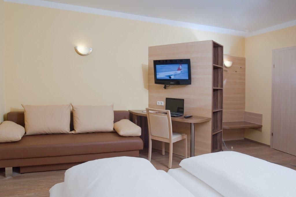 Hotelzimmer mit Sofa, Schreibtisch, Fernseher und Bett.