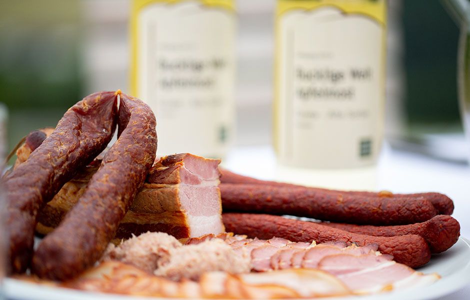 Nahaufnahme von Wurst- und Fleischspezialitäten auf einem Teller mit Flaschen im Hintergrund.