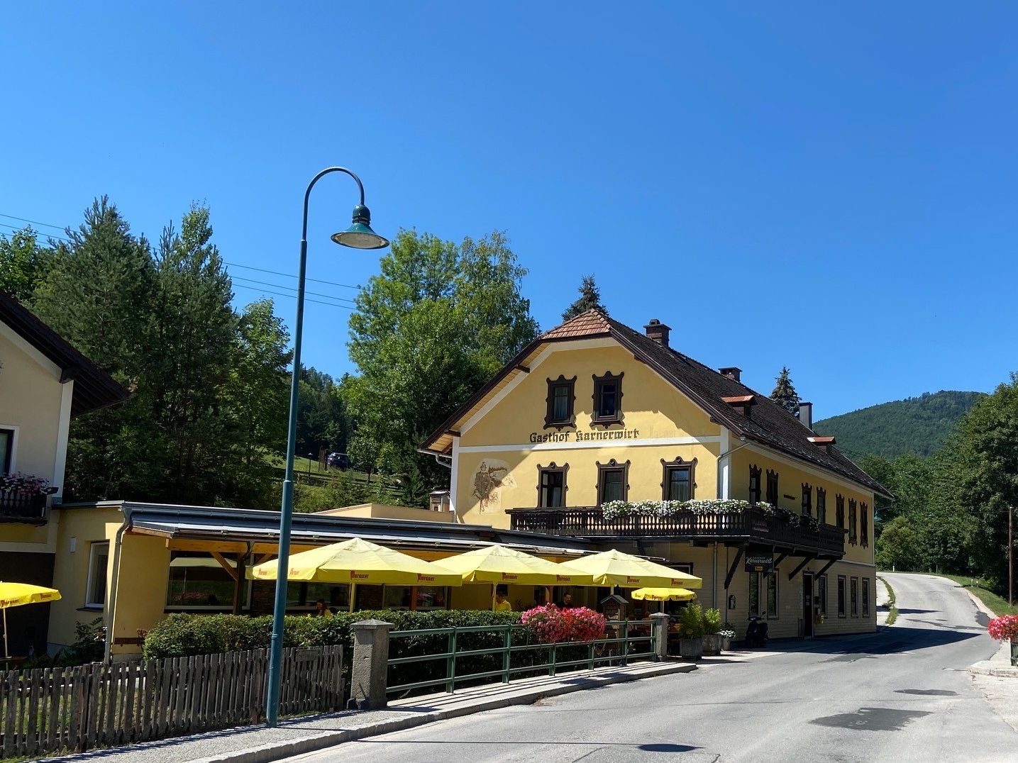 Ein gelber Gasthof mit Balkon und Sonnenschirmen vor einem blauen Himmel.