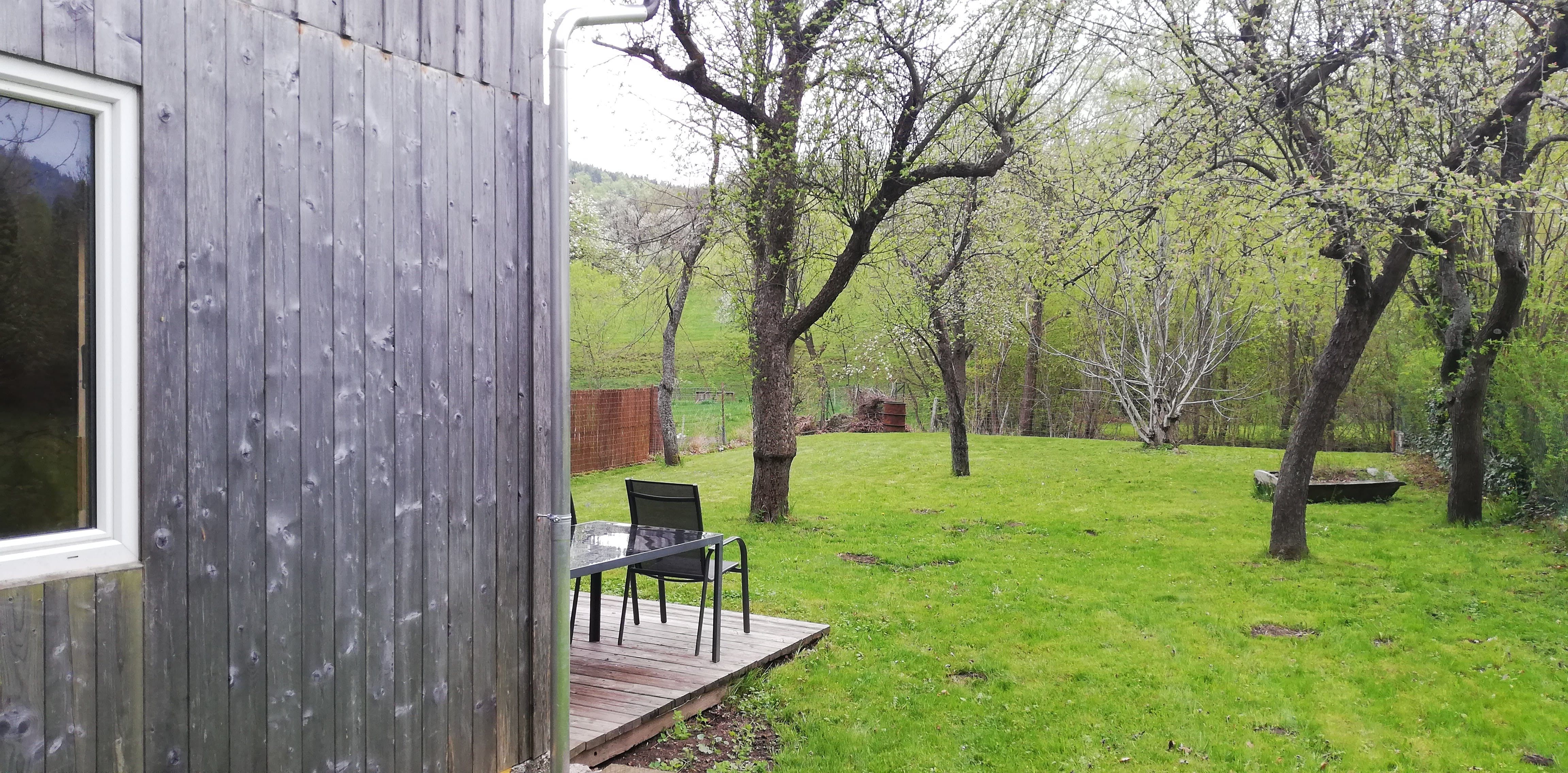 Holzscheune neben Obstgarten mit Tisch und Stühlen auf Holzterrasse.