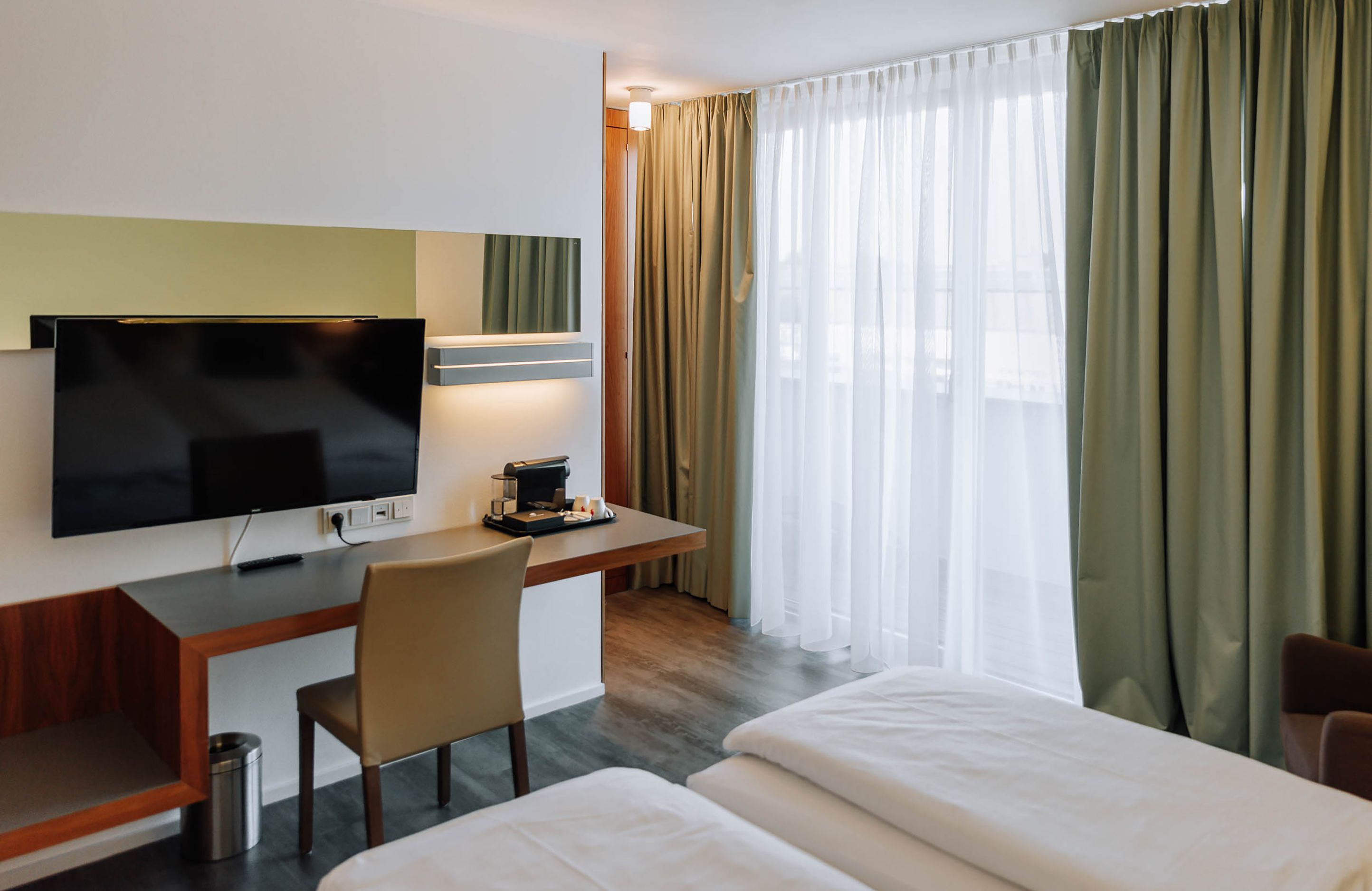 Modernes Hotelzimmer mit Schreibtisch, Fernseher und Vorhängen.