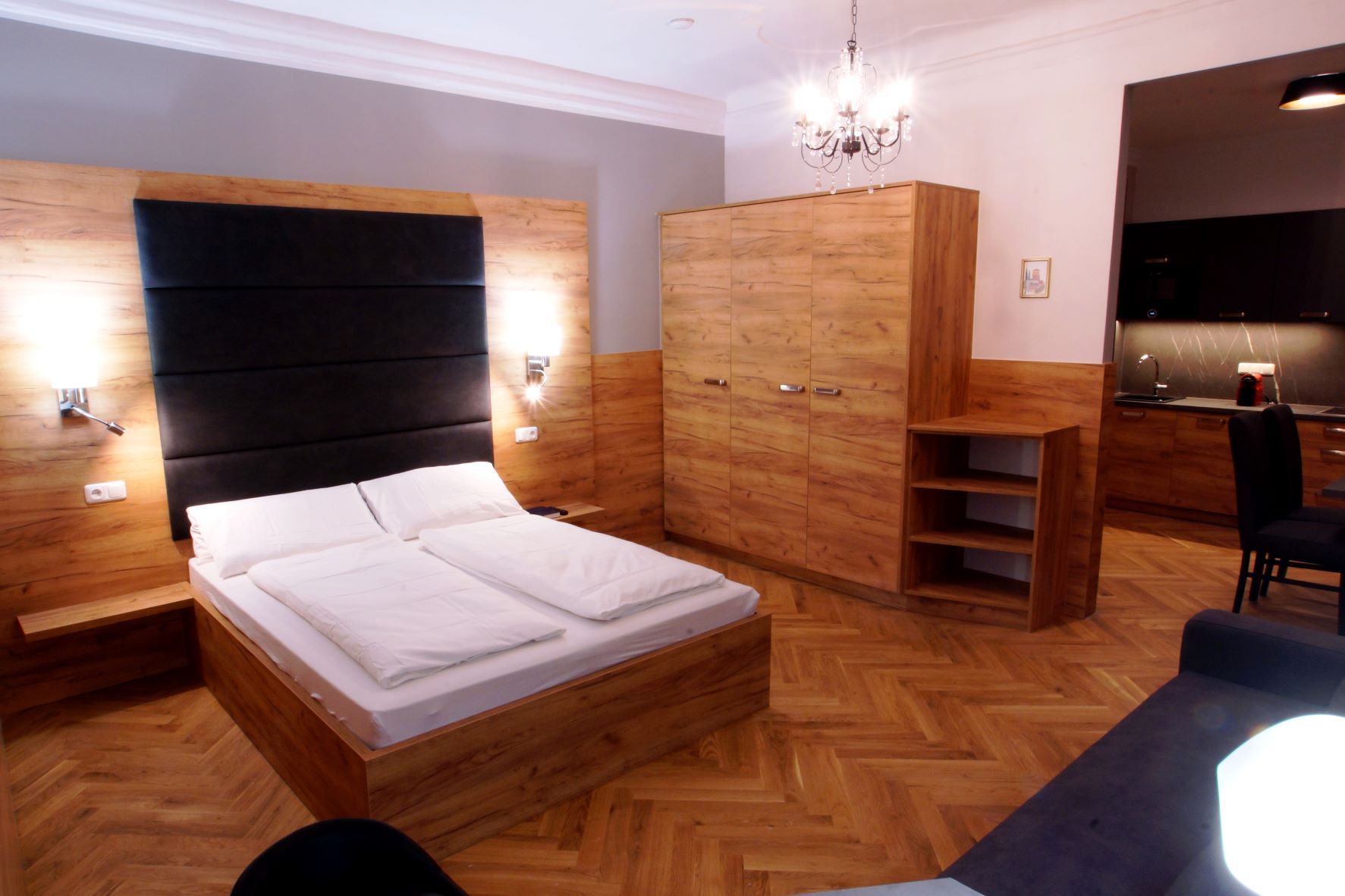 Modernes Apartment mit Holzmöbeln, Doppelbett, Schrank, Kronleuchter und Küchenzeile.