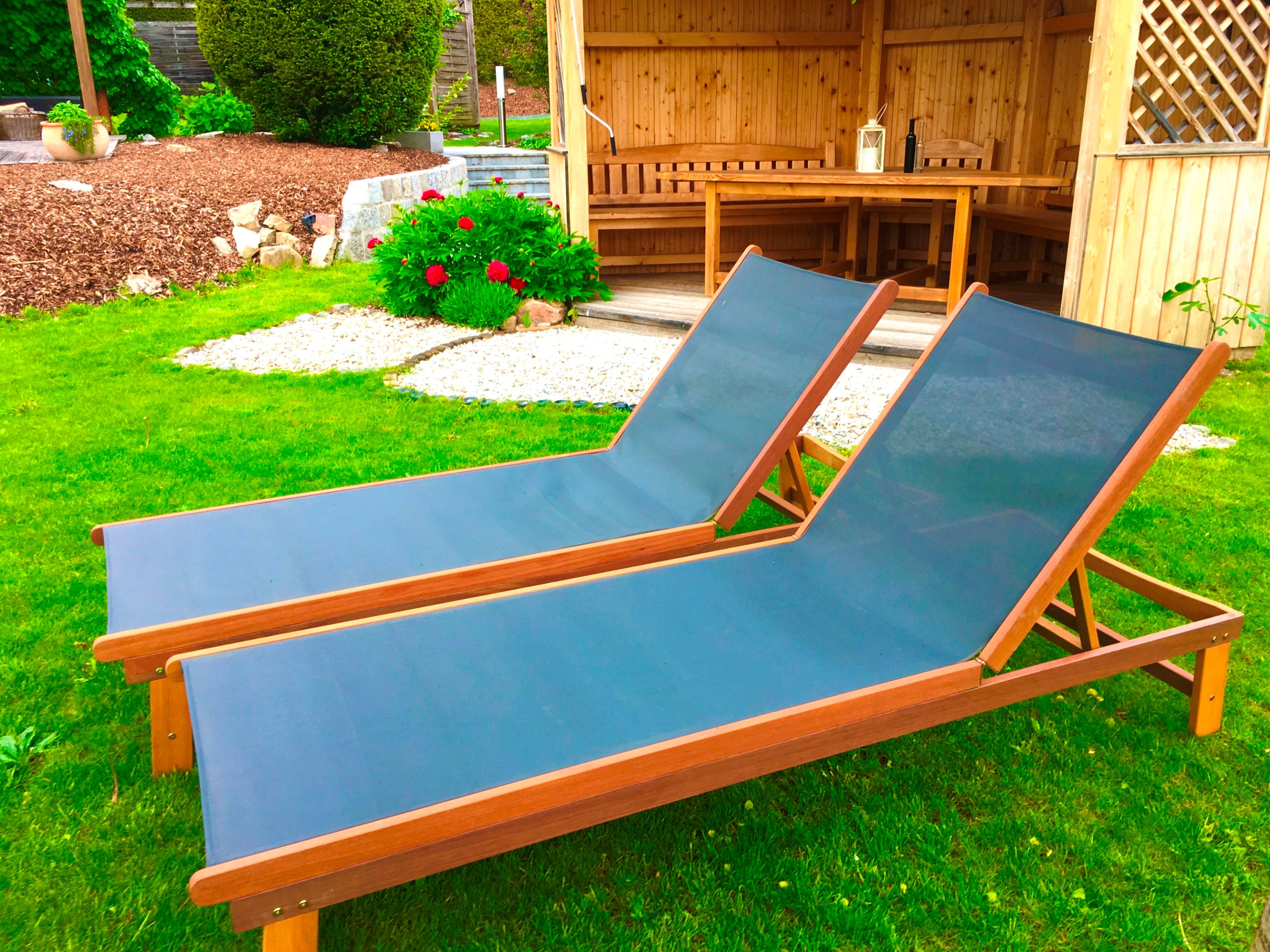 Zwei blaue Liegestühle auf grünem Rasen vor einer Holzhütte im Garten.