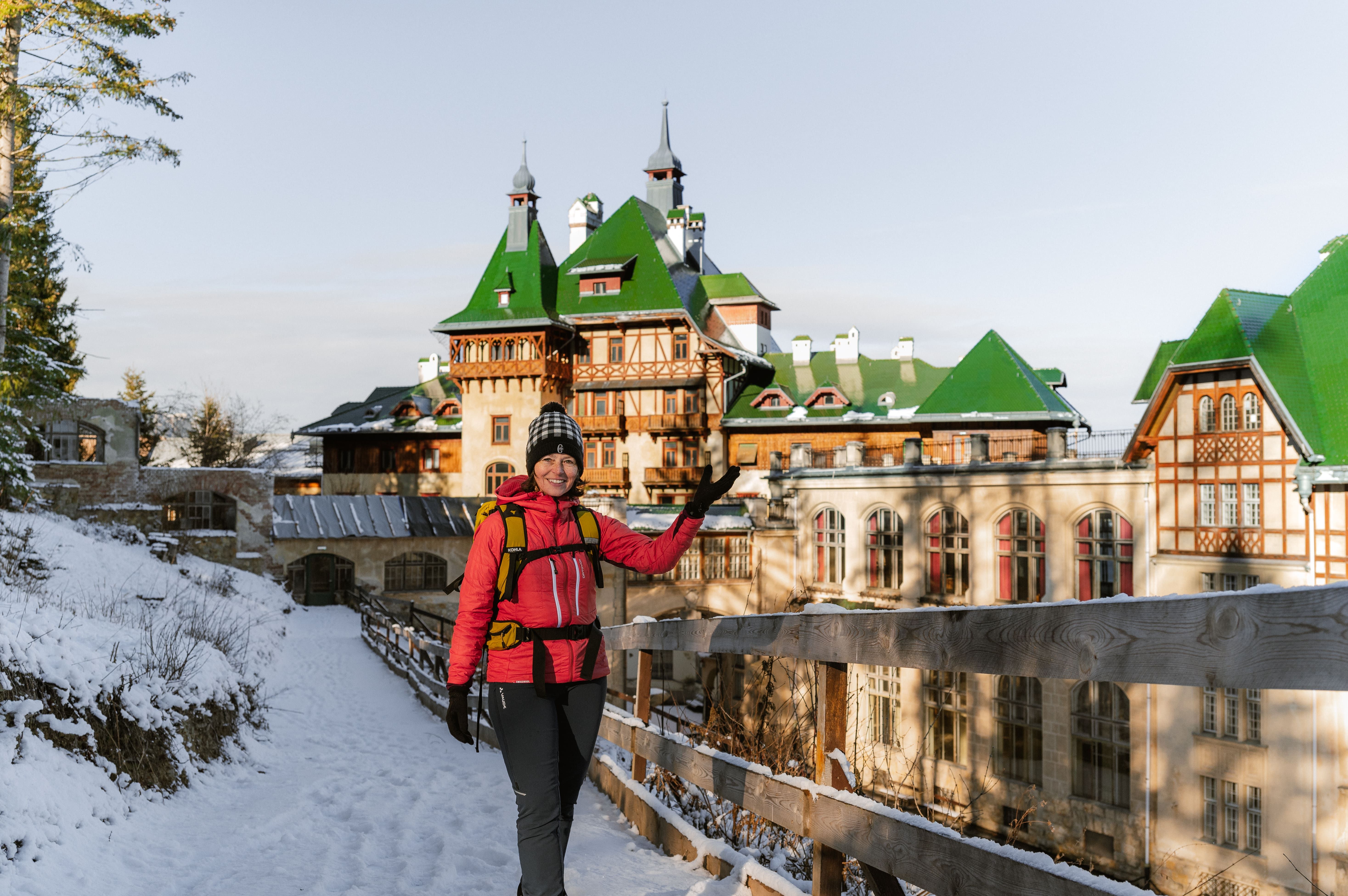 Person in Winterkleidung vor einem großen Gebäude mit grünen Dächern im Schnee.