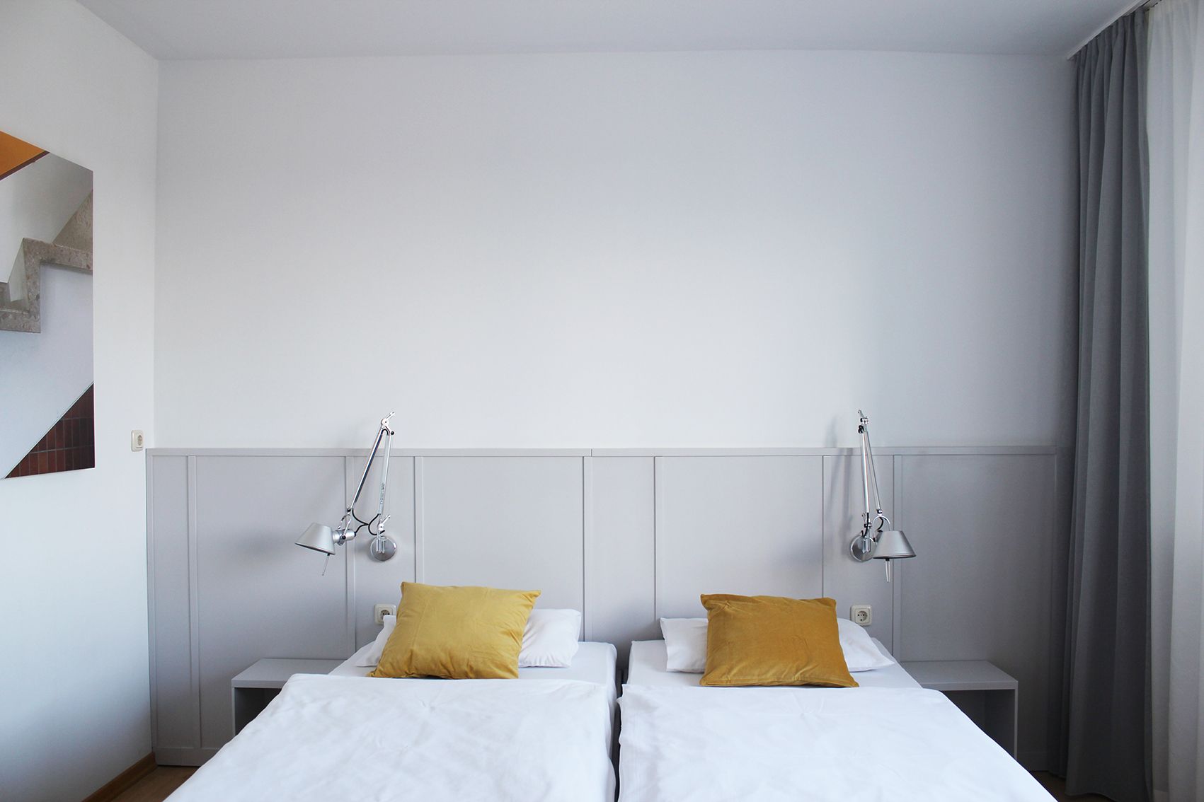 Modernes Gästezimmer mit zwei Einzelbetten, gelben Kissen und Wandlampen.