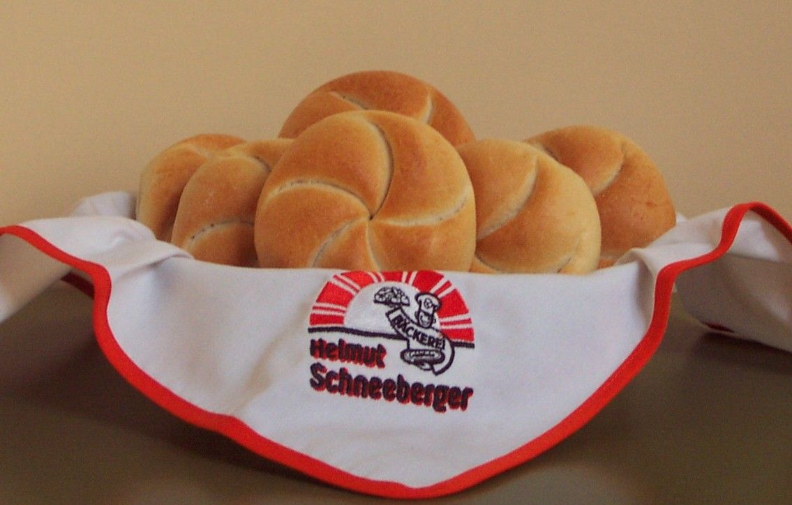 Ein Korb mit frischen Brötchen, bedeckt mit einer Serviette der Bäckerei Helmut Schneeberger.