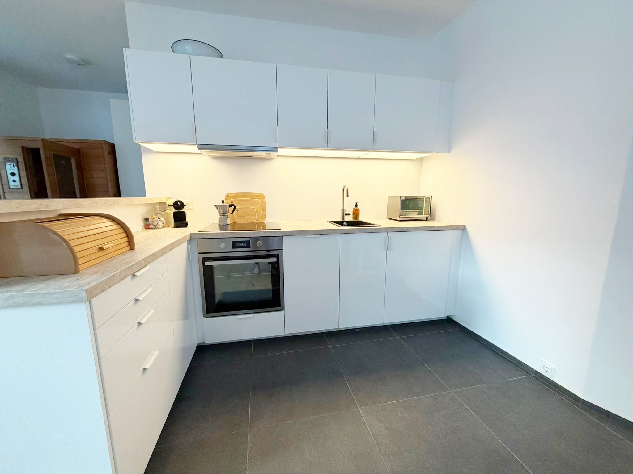 Moderne Küche mit weißen Schränken, Backofen, Spüle und Toaster.