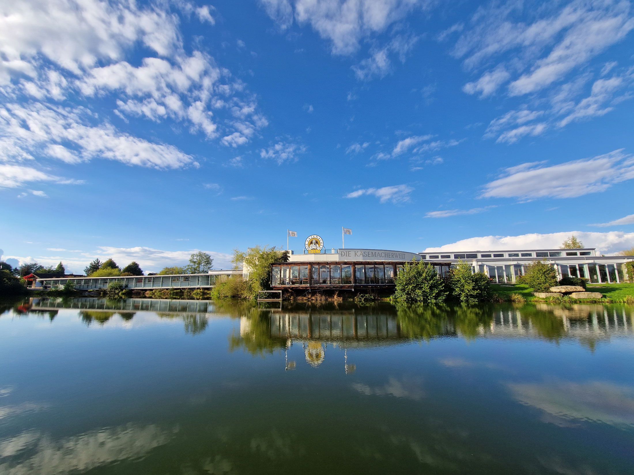 Außenansicht der Käsemacherwelt mit blauem Himmel und See im Vordergrund.