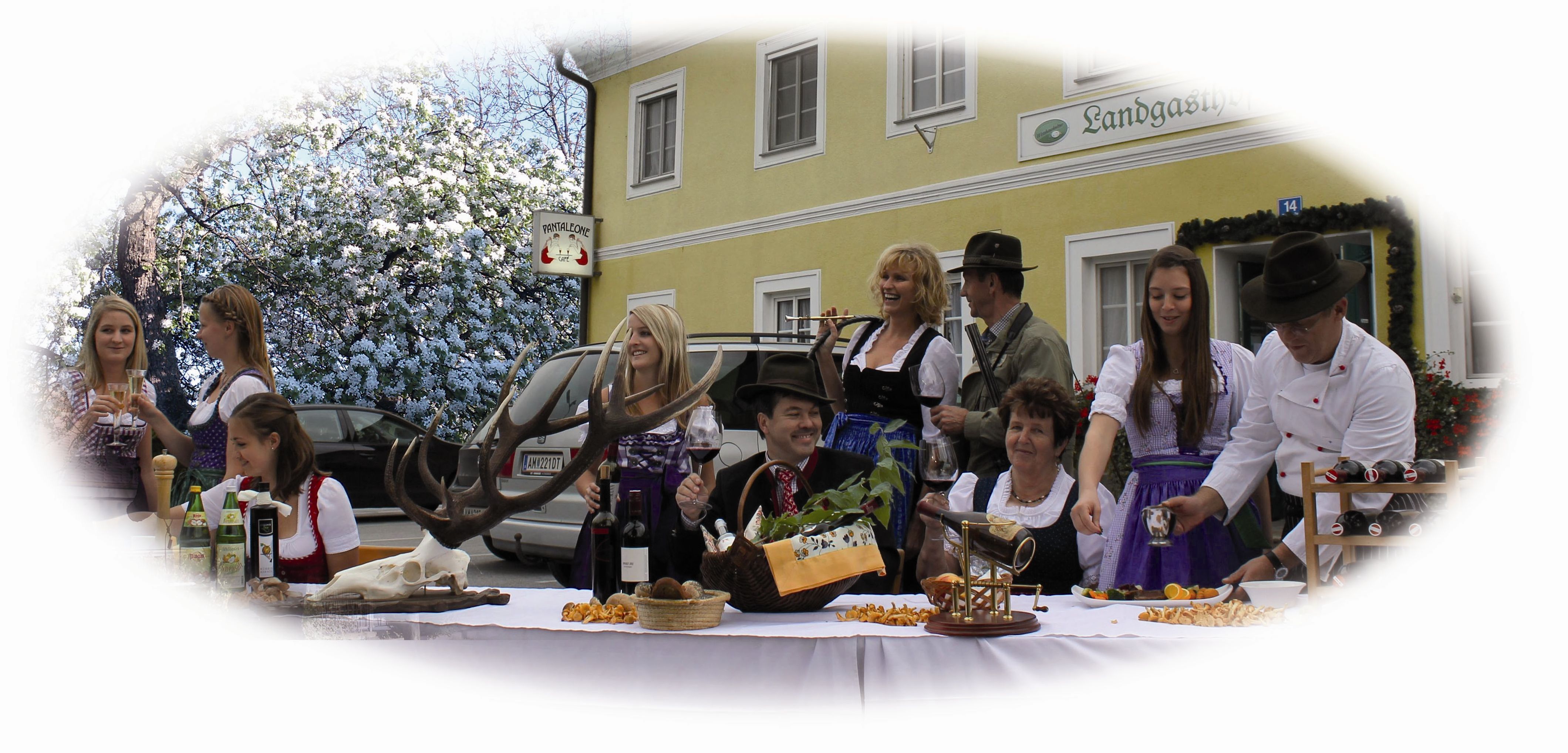 Menschen in Tracht feiern vor einem Landgasthof mit Essen und Getränken.