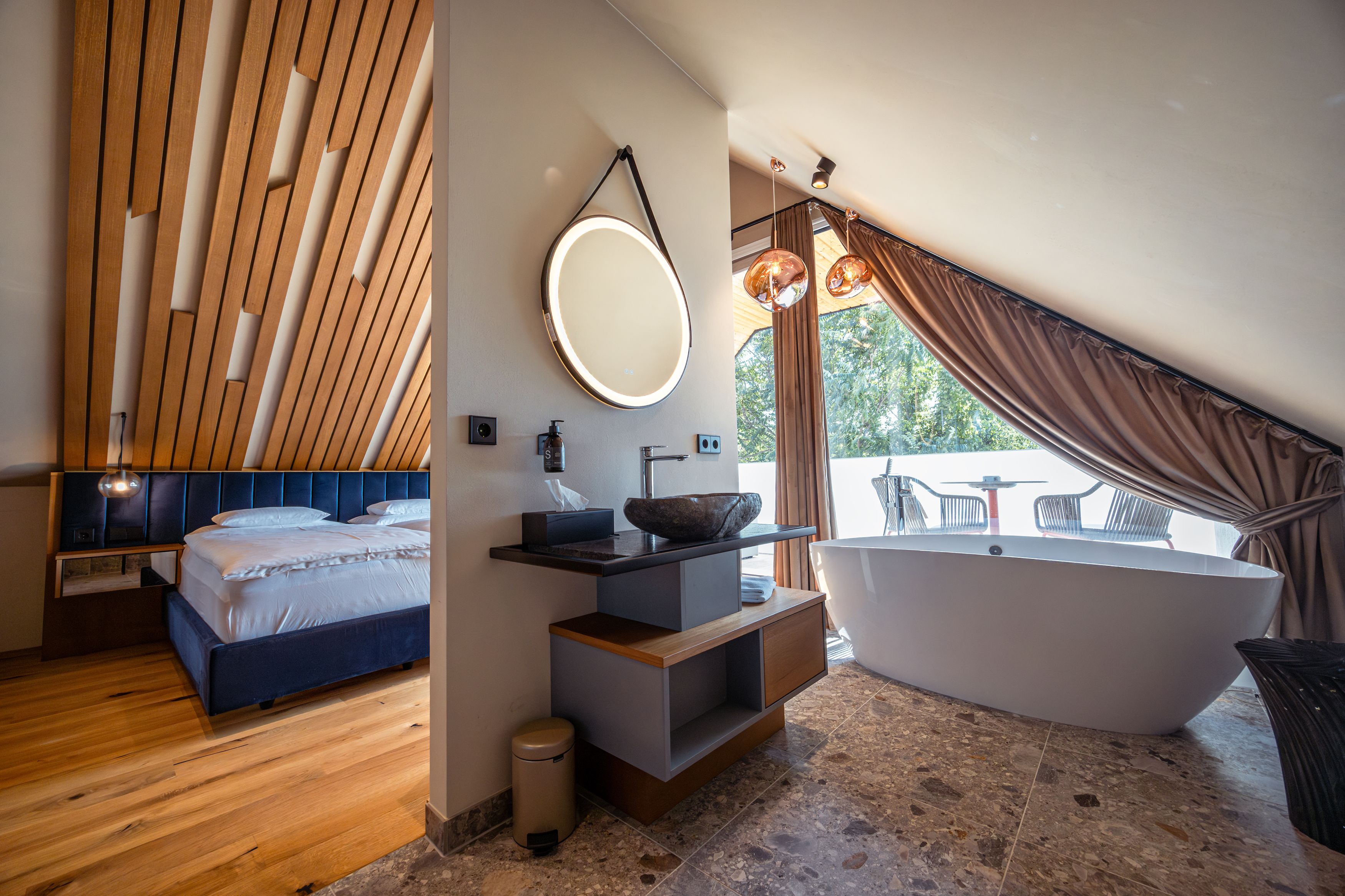 Modernes Hotelzimmer mit Holzdecke, freistehender Badewanne und Balkon.