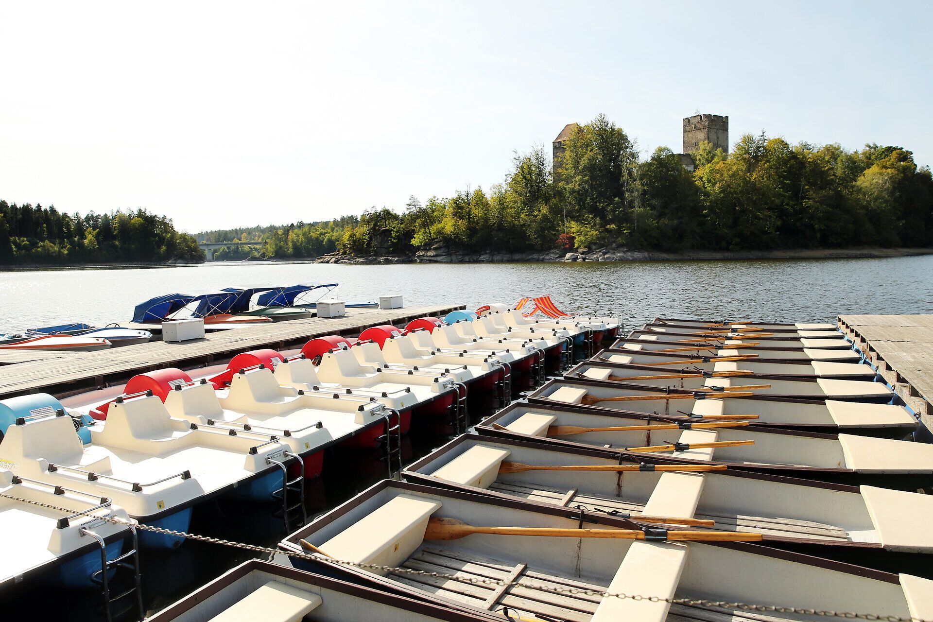 Am Ufer des Stausees Ottenstein reihen sich farbenfrohe Ruderboote aneinander, bereit für unvergessliche Ausflüge auf dem glitzernden Wasser. Umgeben von üppigem Grün und sanften Hügeln lädt die idyllische Landschaft dazu ein, die Seele baumeln zu lassen und die Natur in vollen Zügen zu genießen.