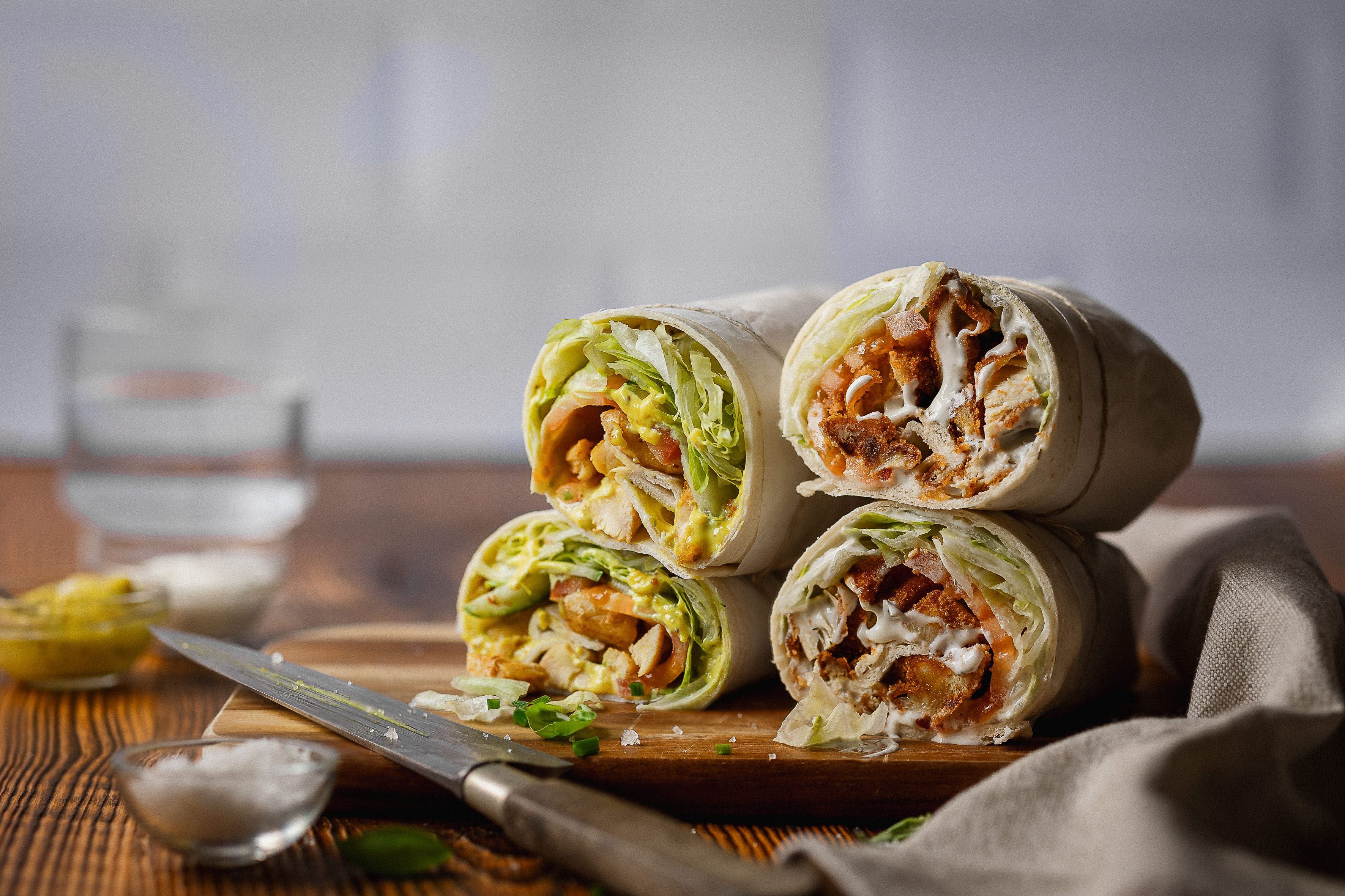 Vier aufgeschnittene Wraps mit Salat und Fleischfüllung auf einem Holzbrett.