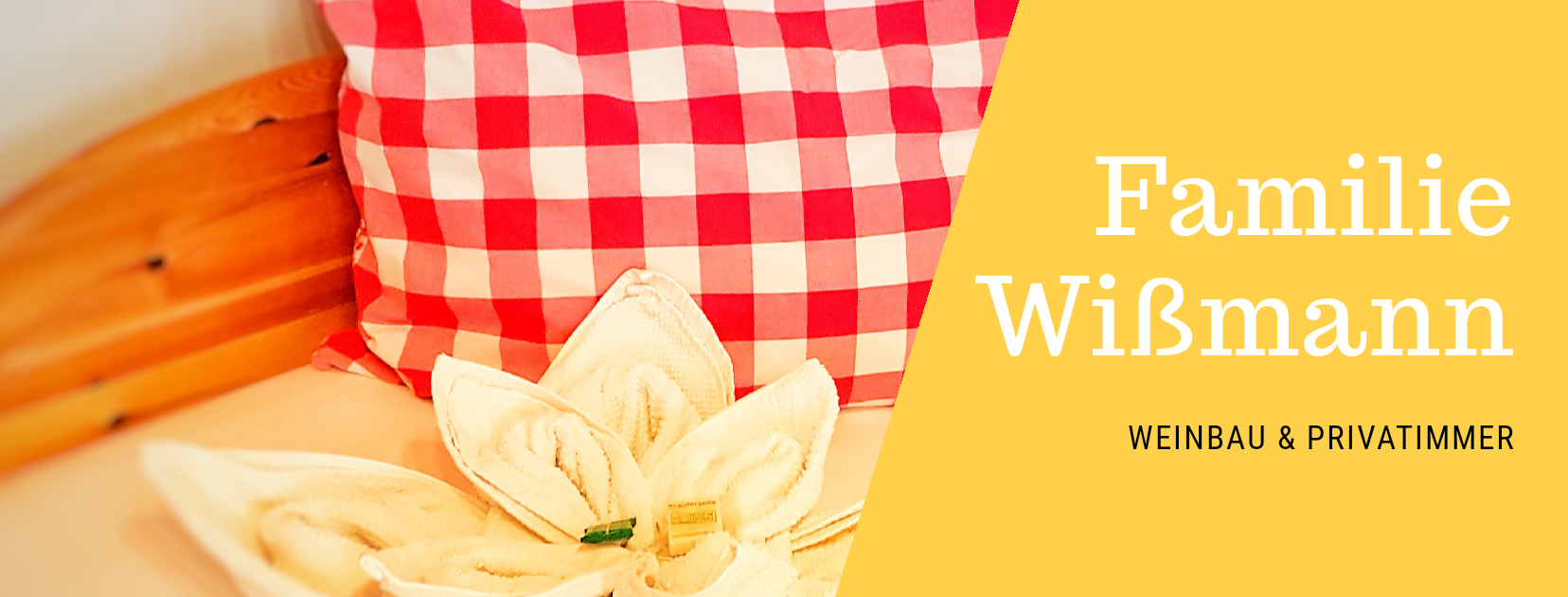 Rotes Kissen mit Karomuster und Handtuch in Blumenform auf einem Bett. Text: Familie Wißmann, Weinbau & Privatzimmer.