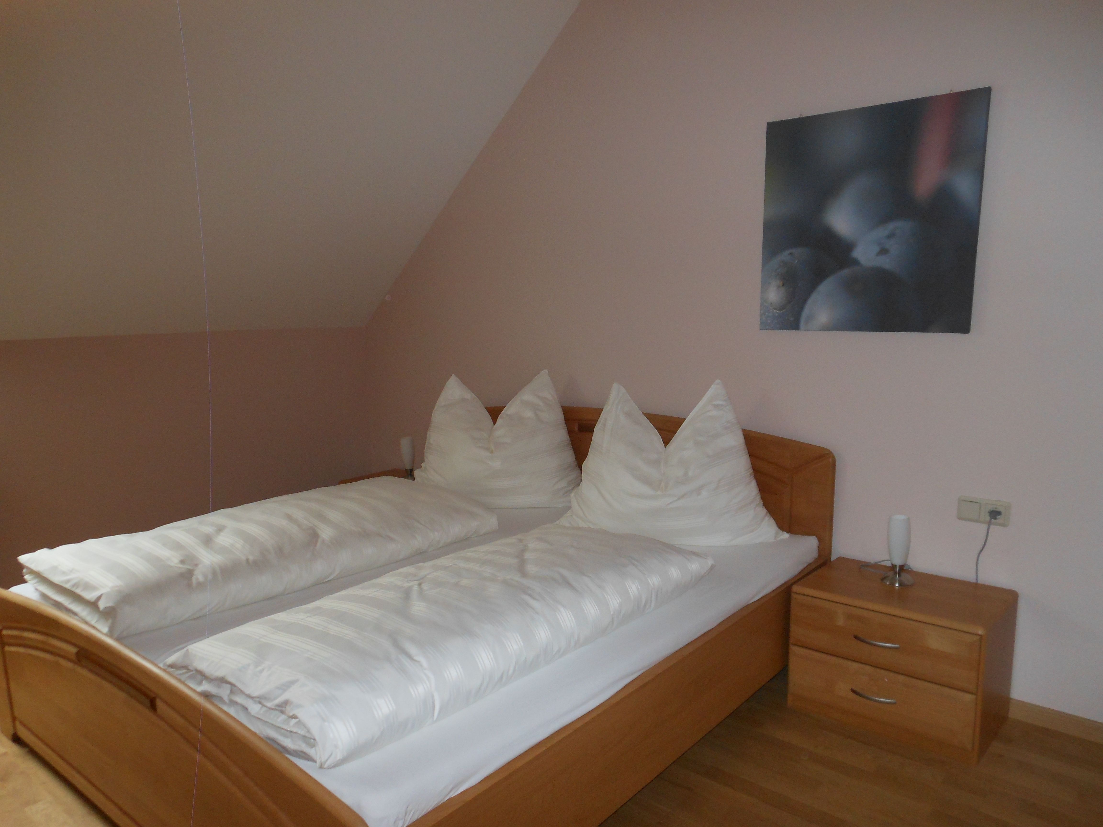 Ein schlichtes Gästezimmer mit einem Doppelbett, weißen Bettdecken und einem Nachttisch mit Lampe.