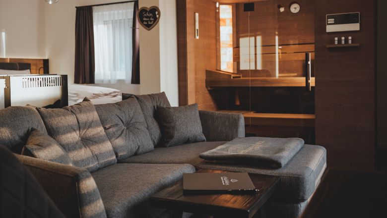 Gemütliches Wohnzimmer mit grauem Sofa und Sauna im Hintergrund.