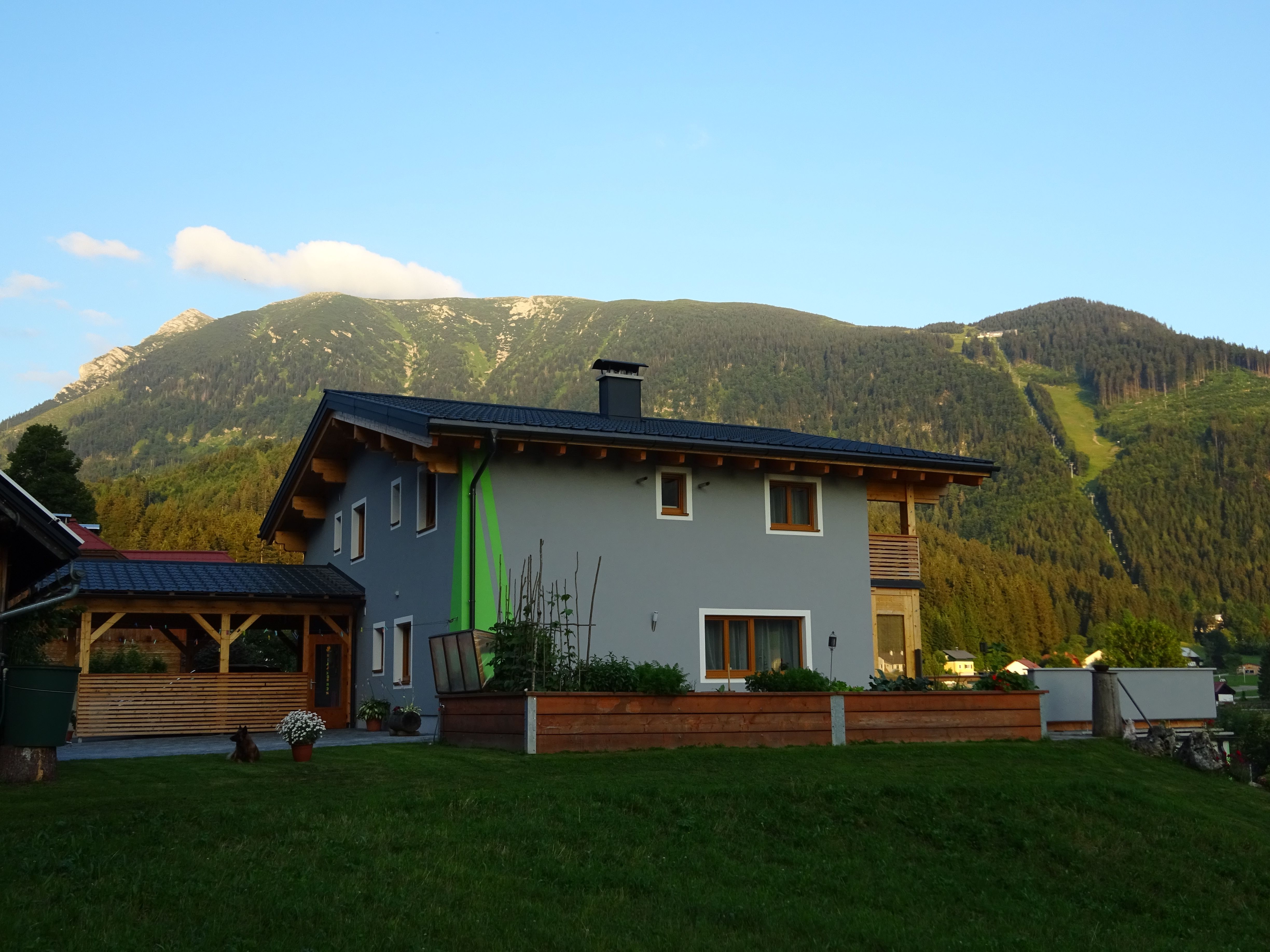 Ein modernes Haus mit grauer Fassade und Holzelementen vor einer Berglandschaft.